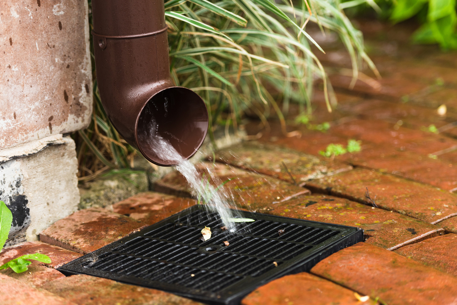 Storm water downspout draining into a catch basin set into brick paving