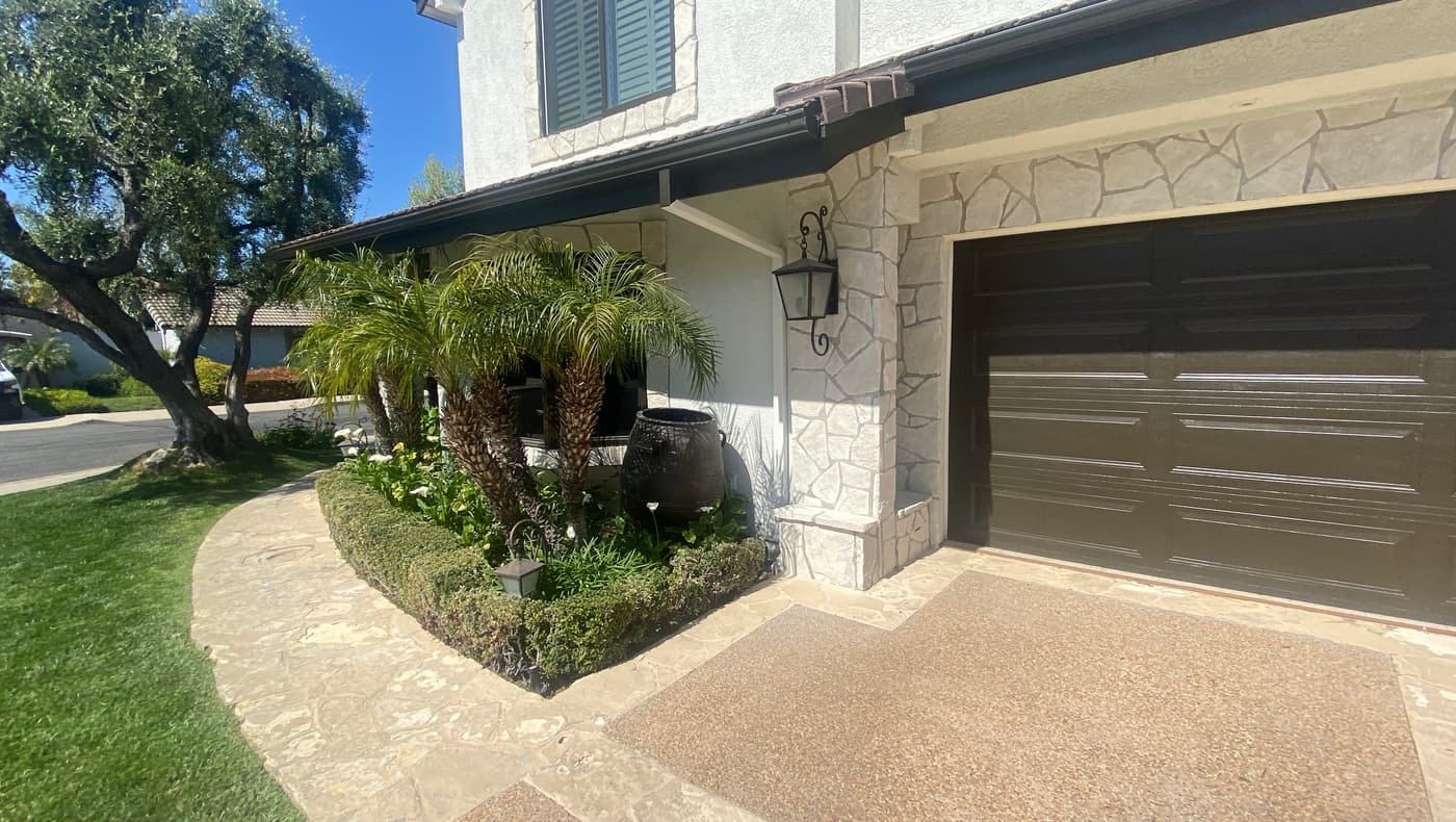 The house before construction, with stone veneer, palms and an urn beside an aggregate walk