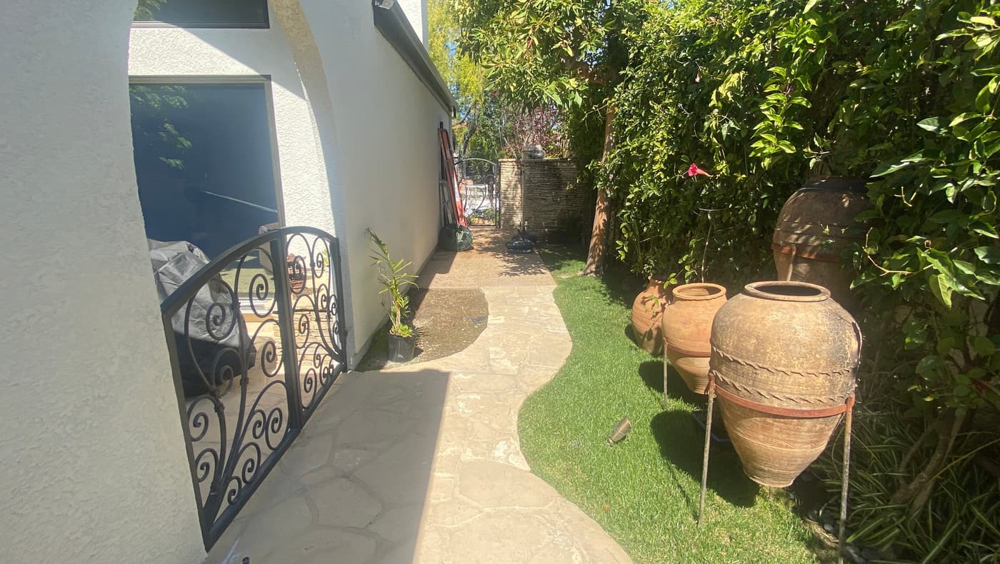 The side courtyard before construction: flagstone paving, a strip of lawn, terracotta urns and a wrought iron gate