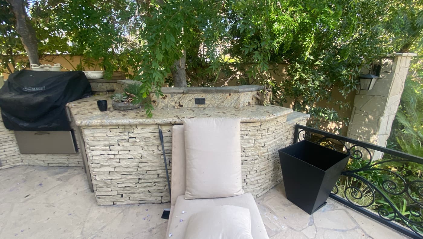 The existing stacked stone bar with its granite top and cushions, under a mature tree