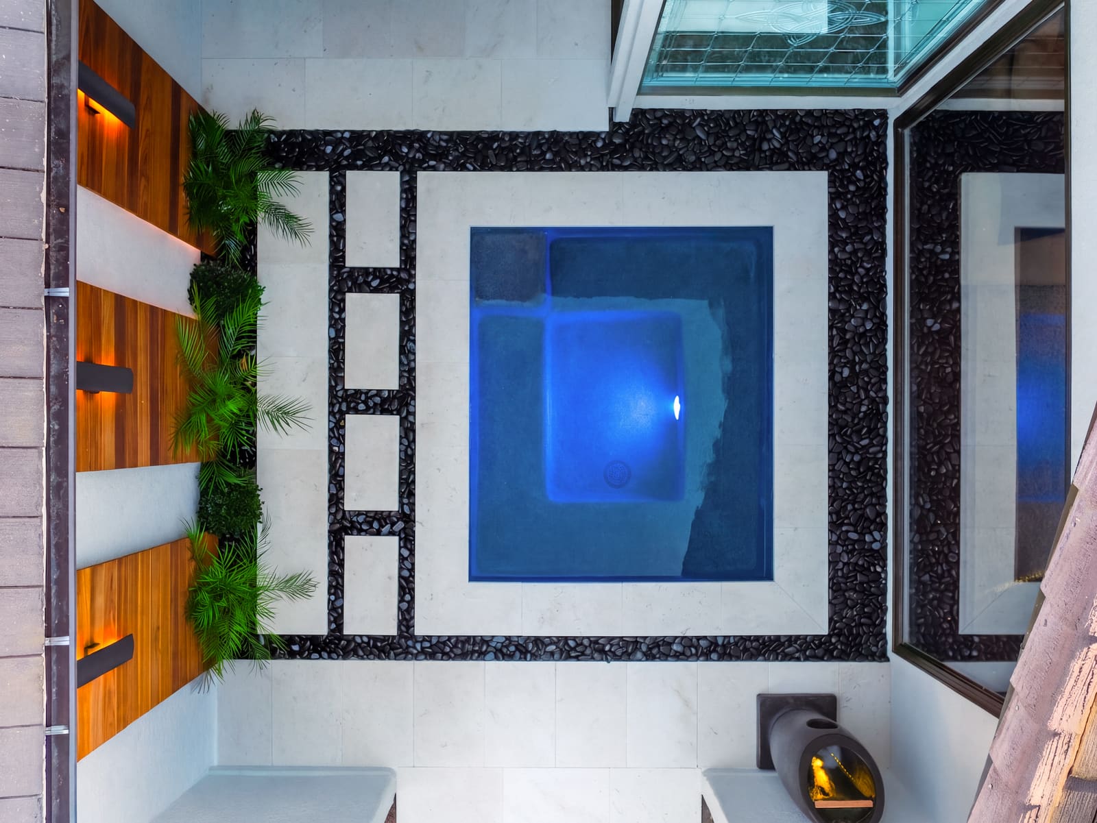 Aerial view of the courtyard, with the spa set among pale stone steppers and black pebble joints, framed by cedar slat walls
