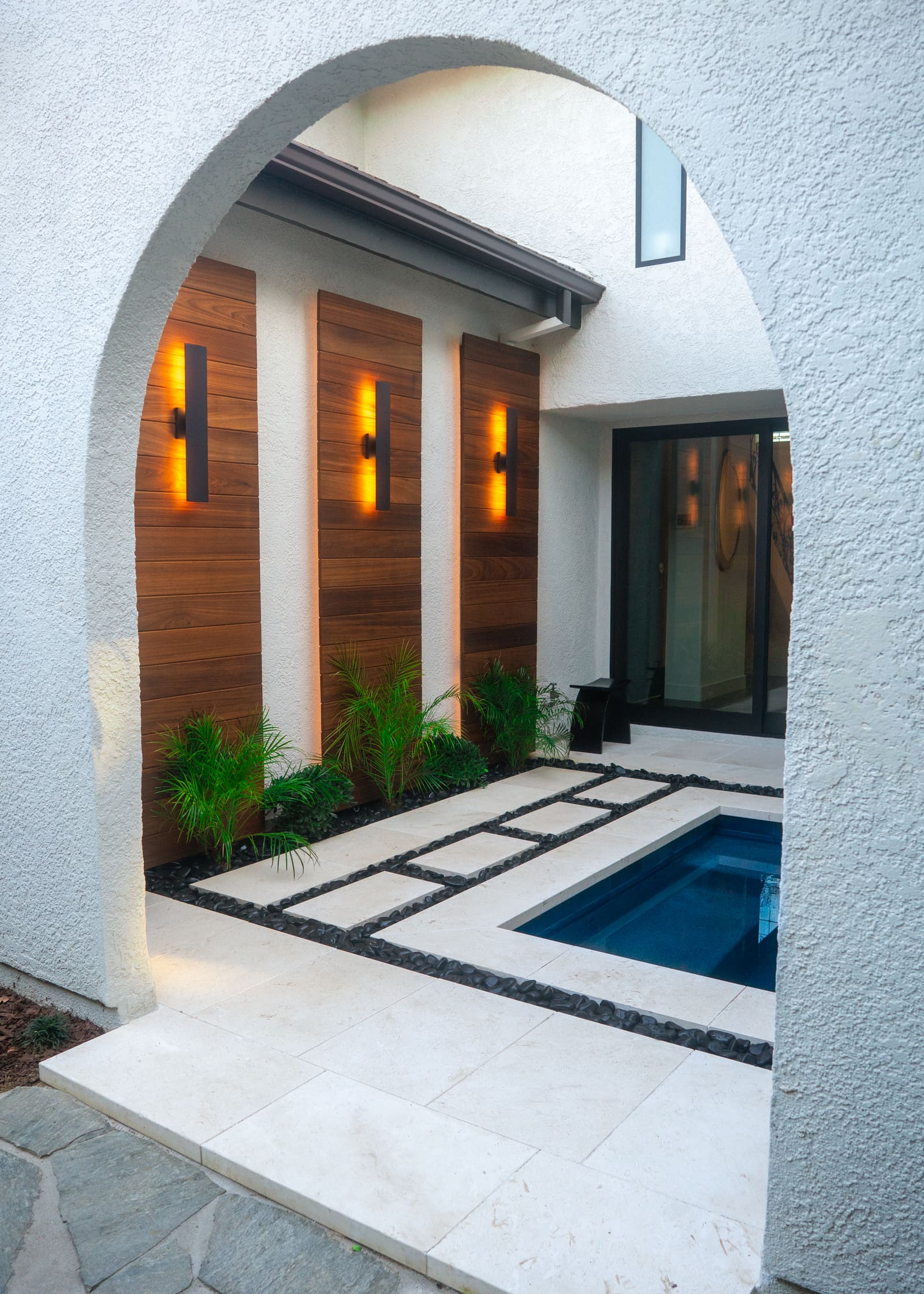 Stucco arch opening onto the courtyard, with the spa, cedar slat panels and lit sconces beyond