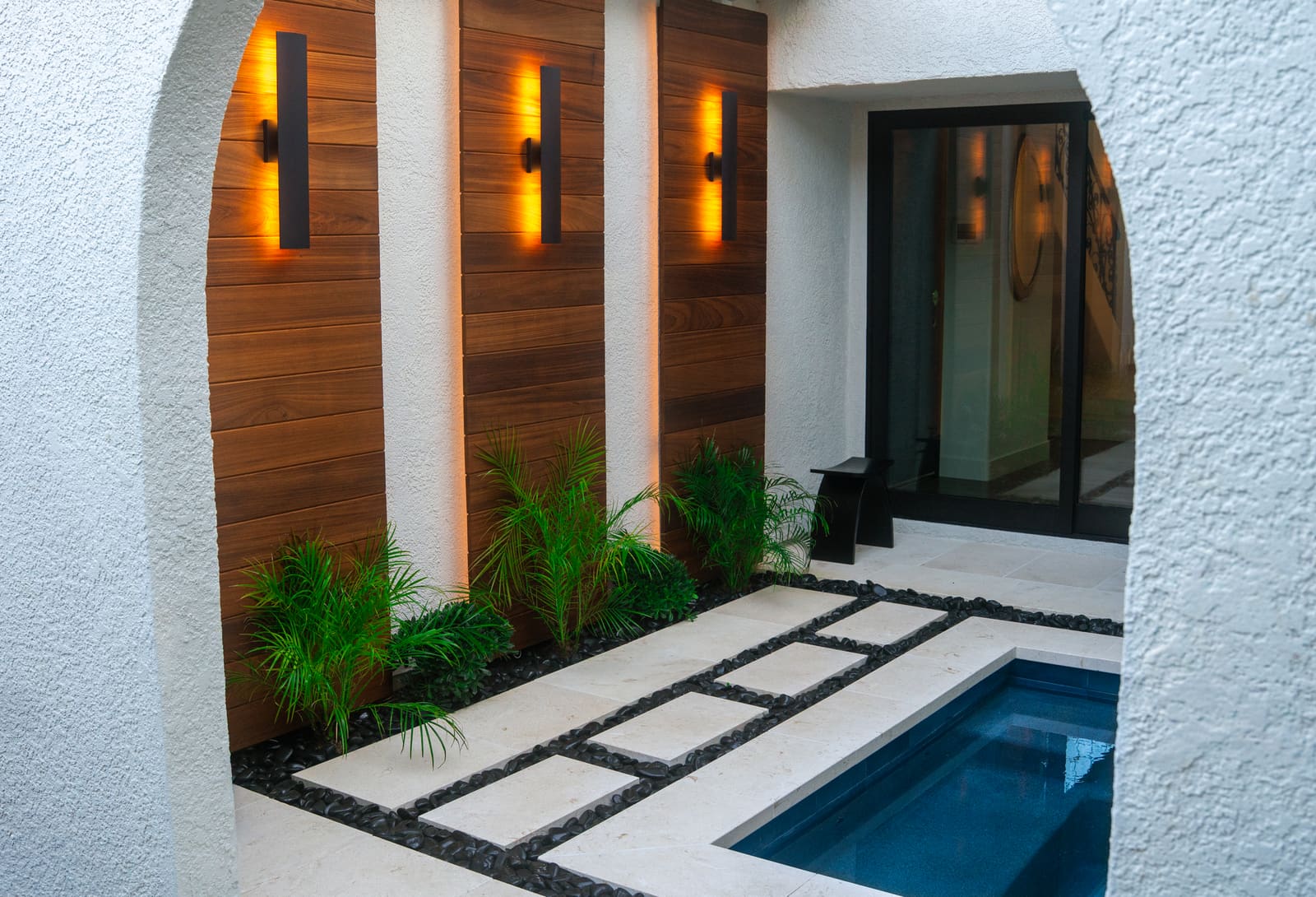 Cedar slat panels with black linear sconces along the courtyard wall beside the spa