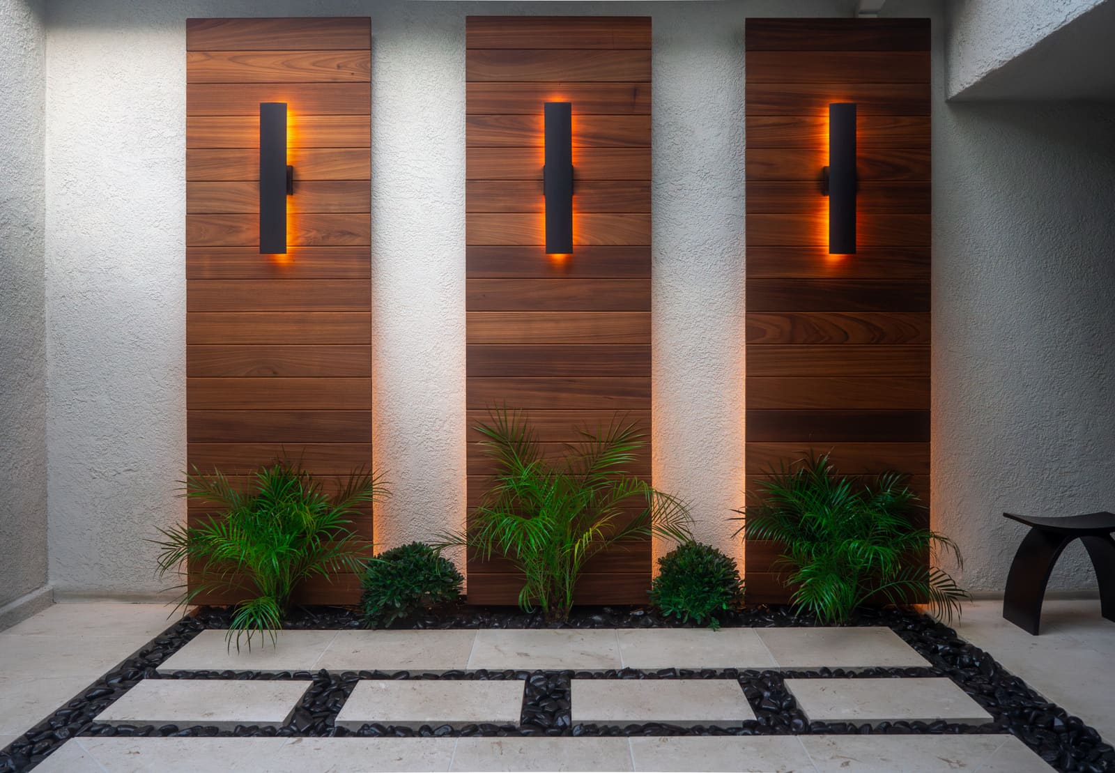 Three cedar panels lit from above by wall sconces, over beds of foxtail fern and dwarf mondo grass