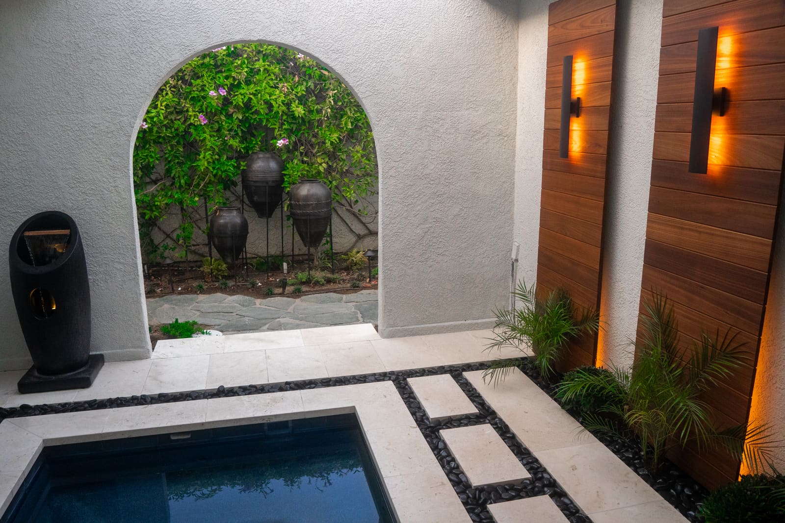 Arched opening framing bougainvillea trained on a trellis, with hanging urn fountains beyond