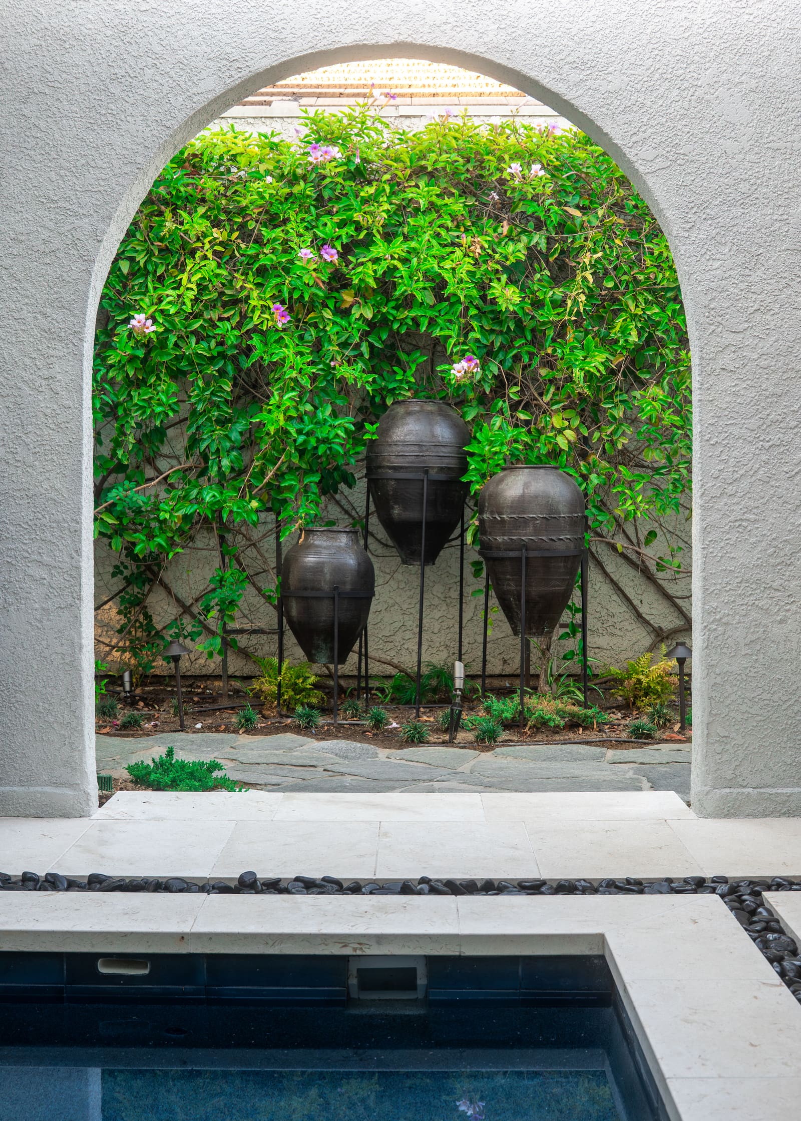 Two dark ceramic urn fountains hung on the wall beneath flowering bougainvillea