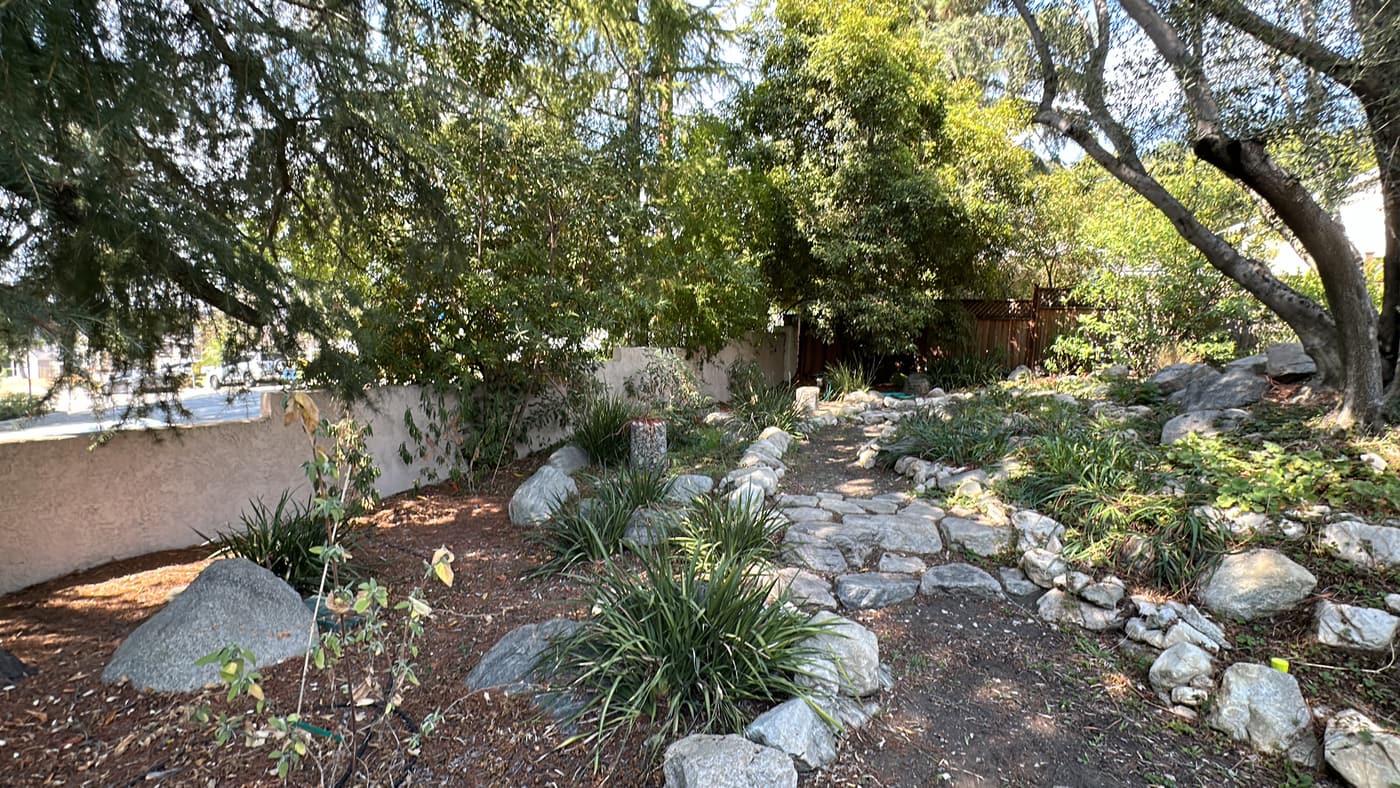 The existing dry creek bed before construction, lined with boulders and mulch under mature trees
