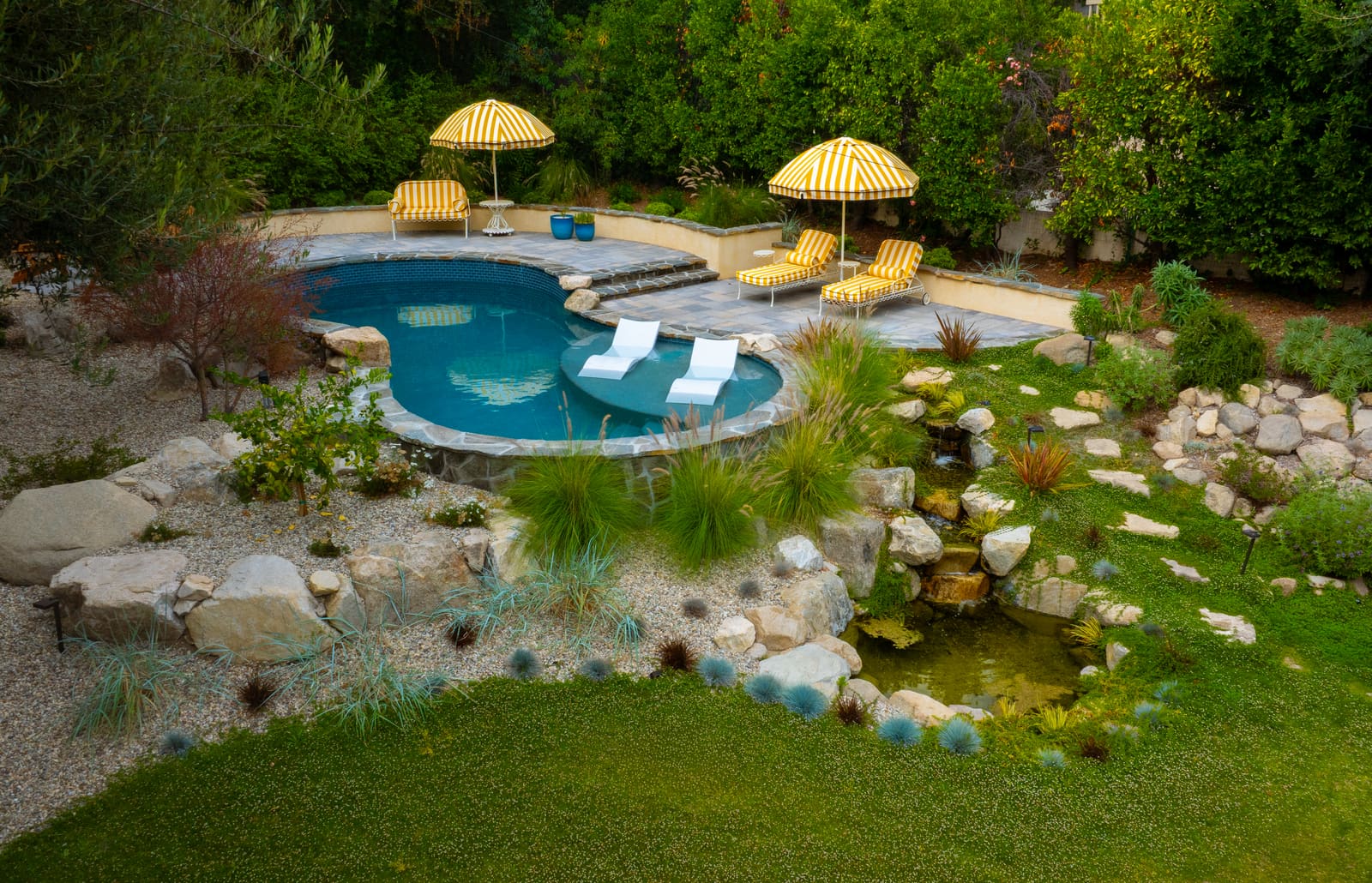 The freeform pool with striped umbrellas and loungers, boulder coping and grasses along the water