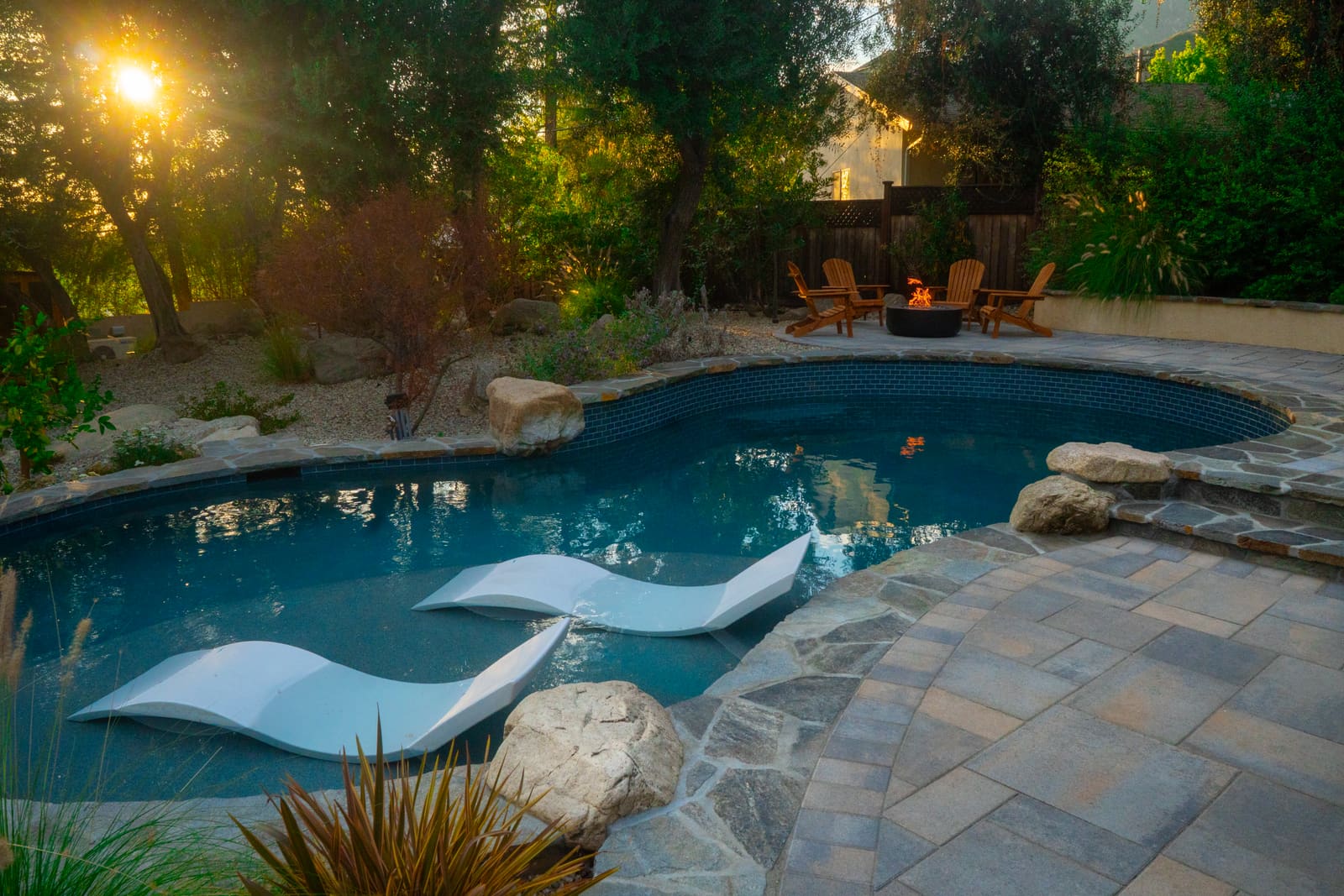 In-pool loungers on the shelf of the freeform pool, with flagstone decking and boulders beyond
