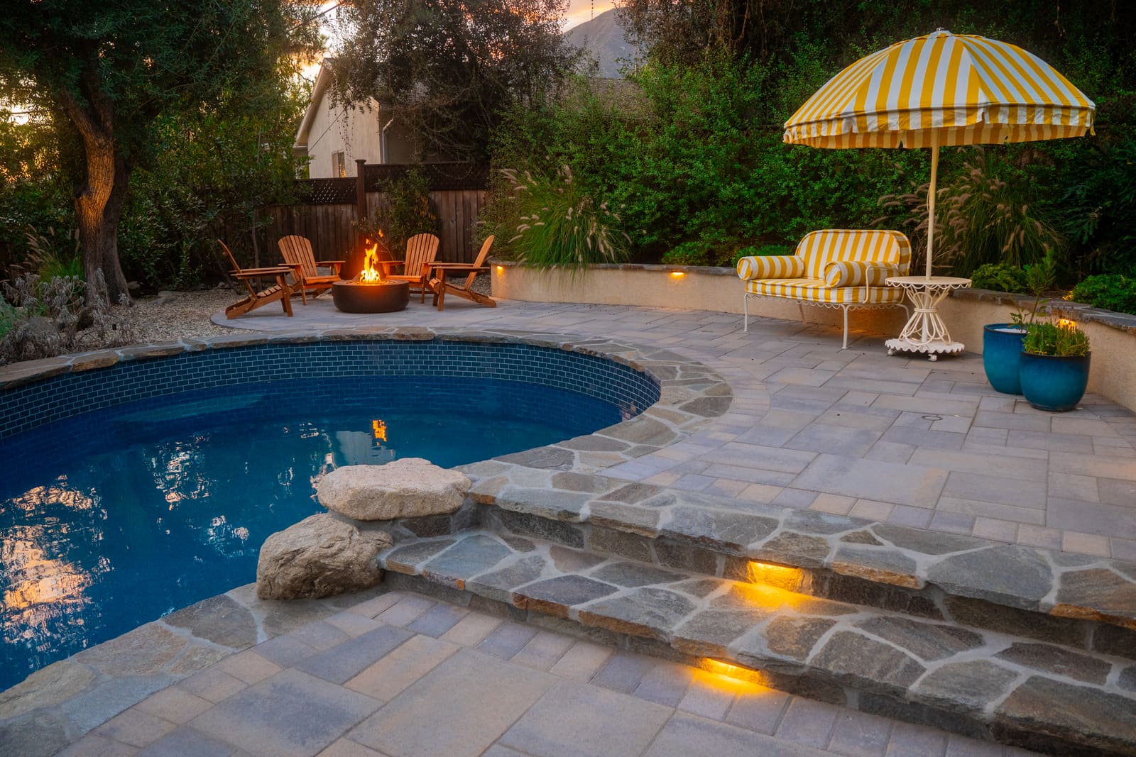 Circular gas fire bowl on the flagstone patio, ringed with wooden Adirondack chairs