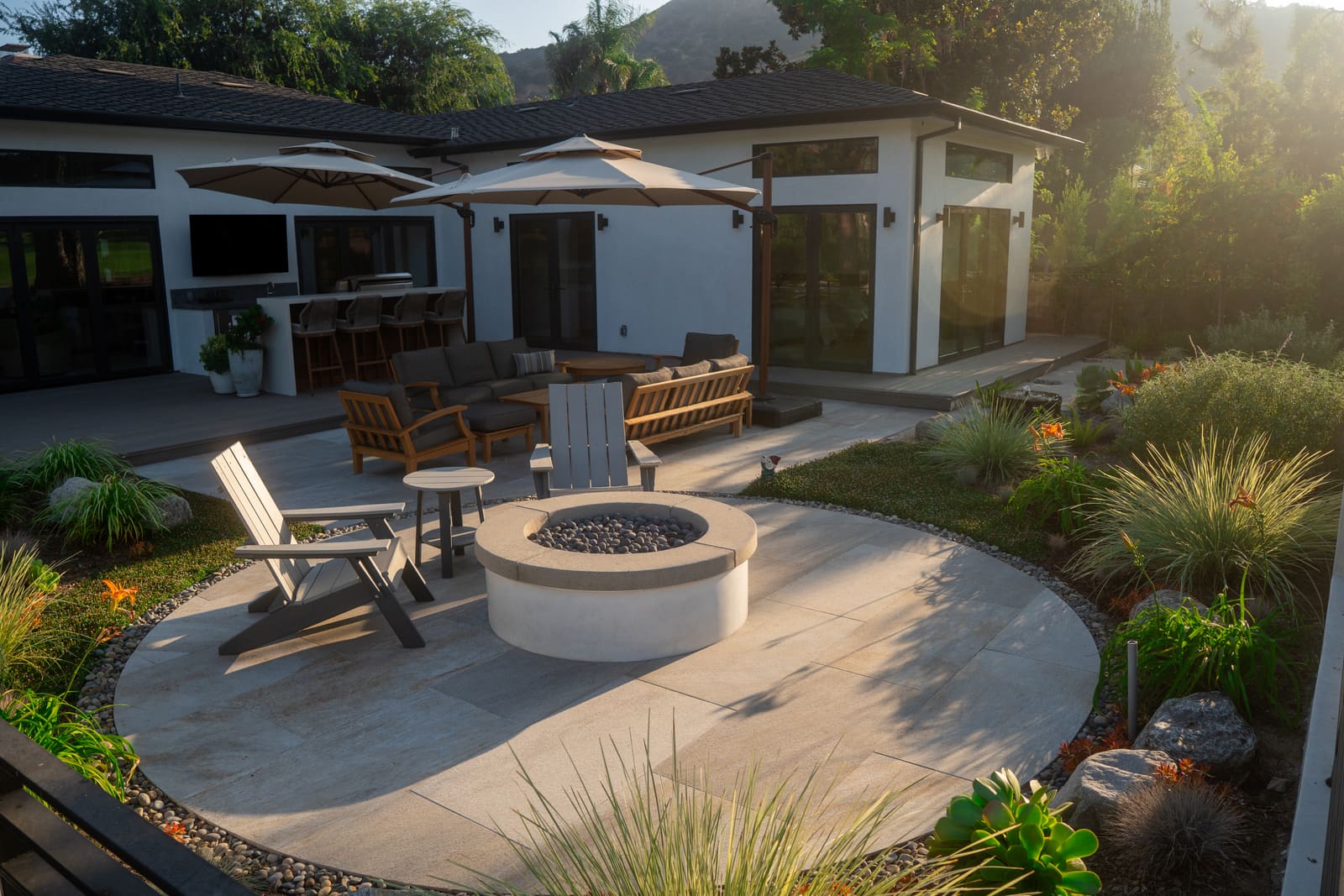 The curved concrete patio and fire pit at golden hour, with the outdoor kitchen and bar under the roofline