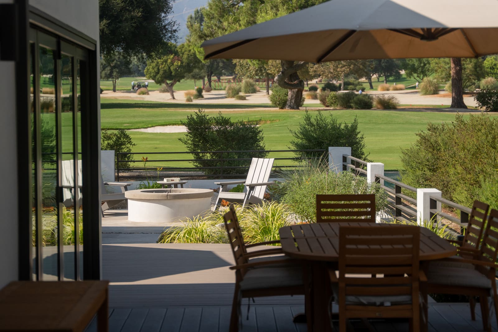 Dining table and umbrella on the deck above the patio, with the fairway beyond the cable rail