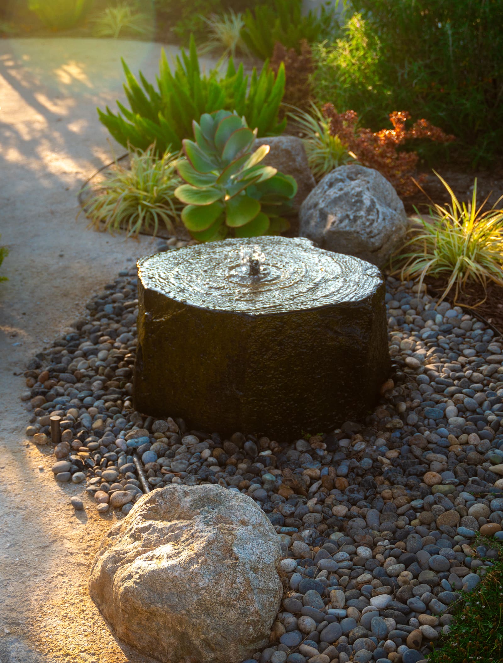 Succulents and air plants around a core-drilled stone fountain in a cobble bed