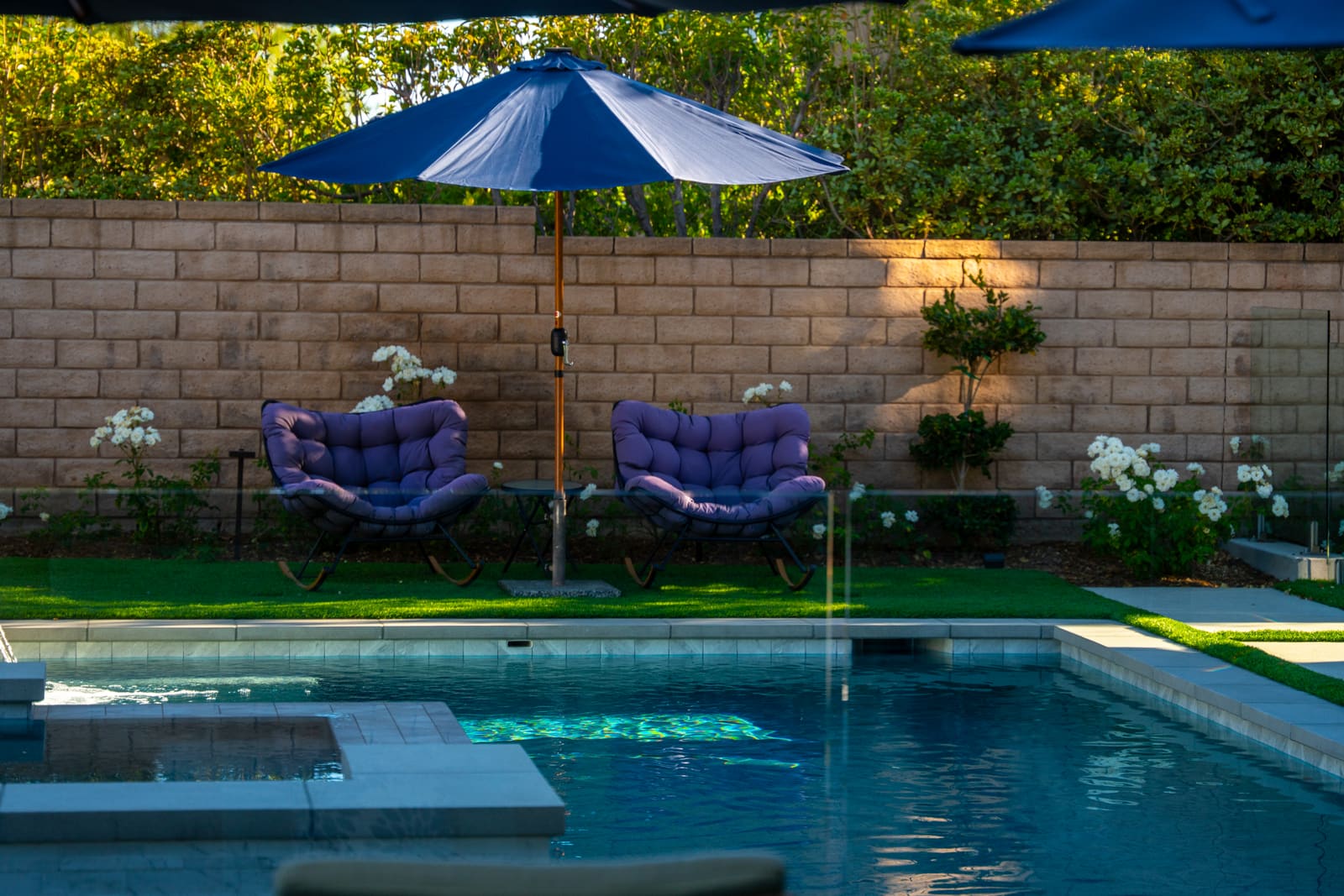 Loungers under a navy umbrella on the turf beside the pool and raised spa