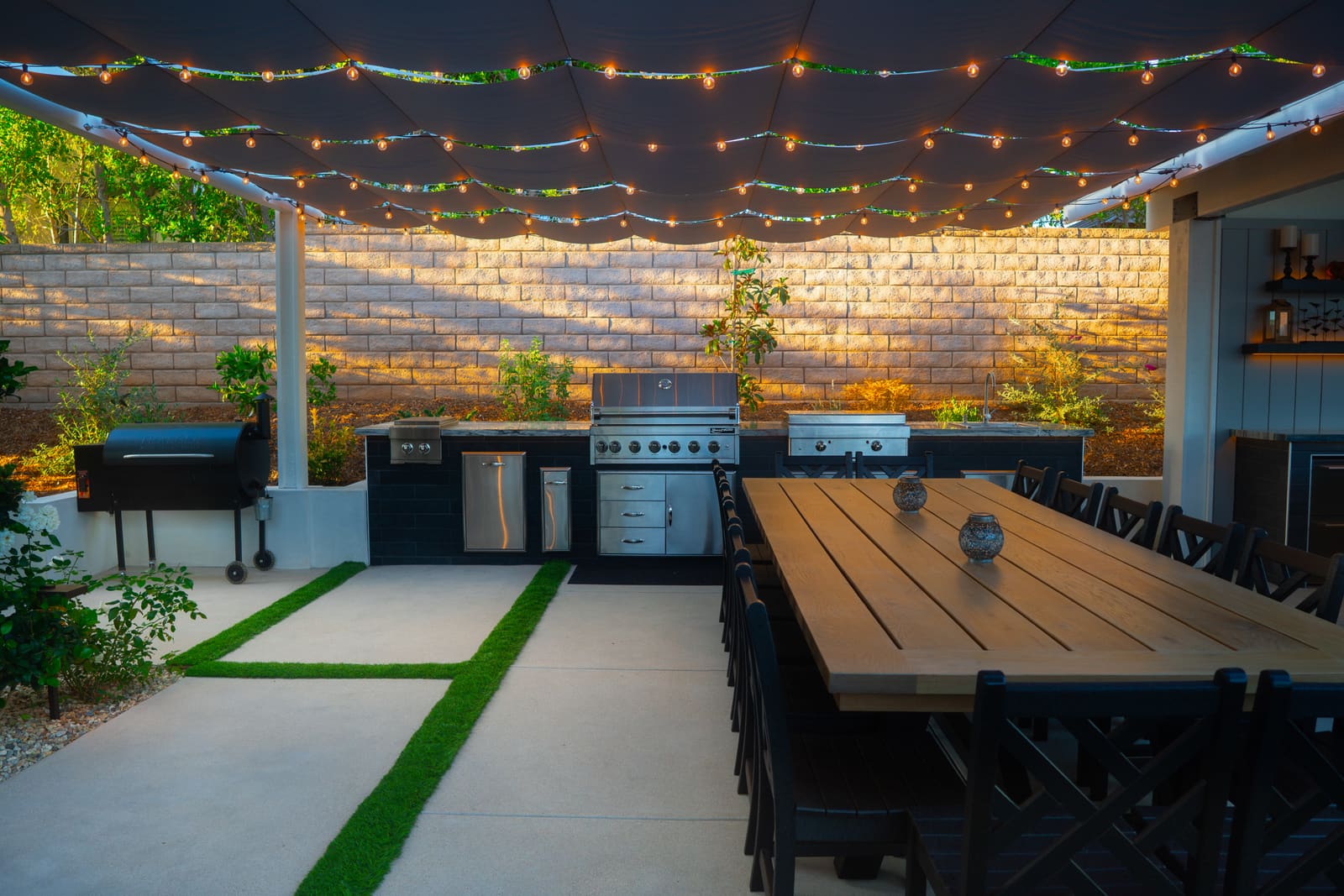 String lights over the long dining table, with the kitchen run and split-face block wall behind