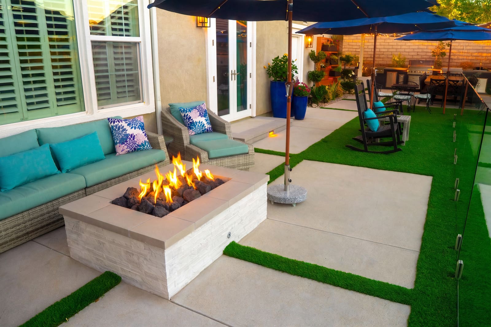Gas fire table alight between cushioned benches, on concrete paving with turf joints