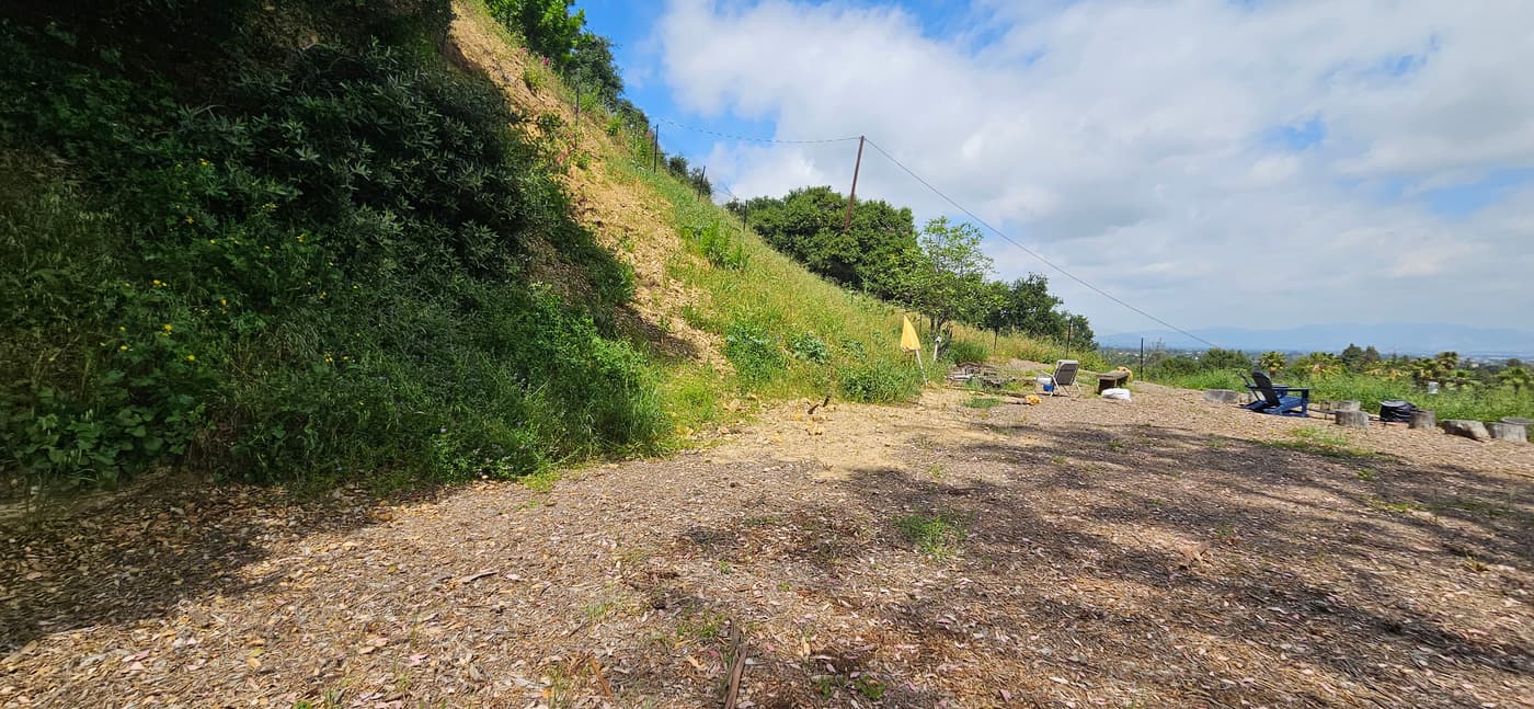 The foot of the slope before construction, bare ground below a grassy hillside and wire fence