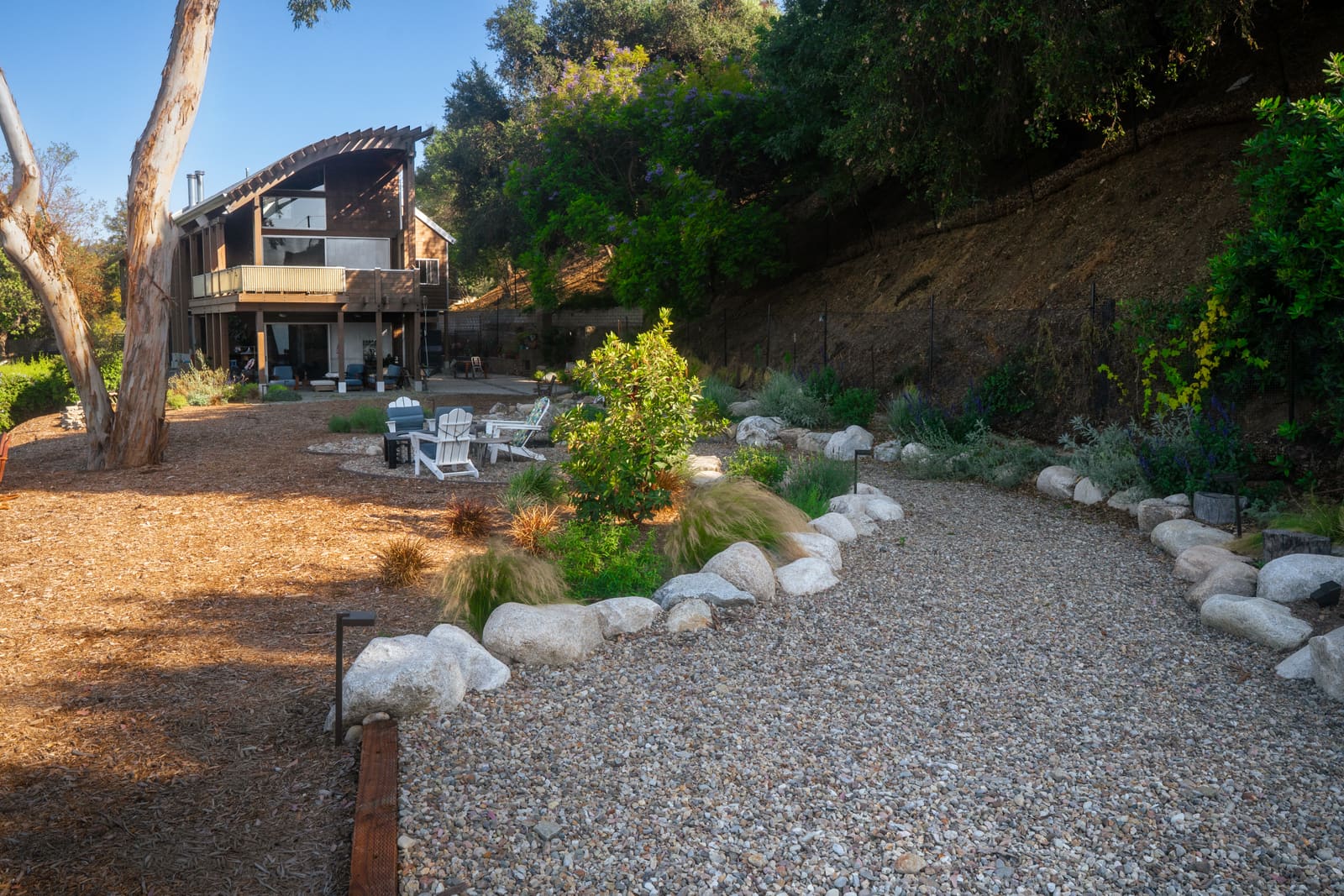The house and deck above the hillside garden, with boulder-edged beds and grasses on the slope