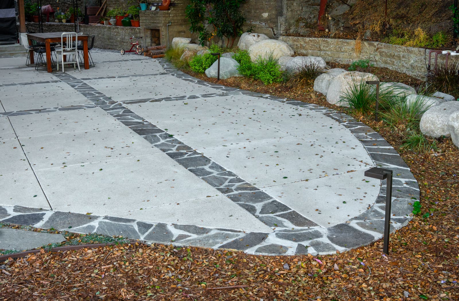 Concrete paving banded with flagstone and pebble, leading between boulders and grasses