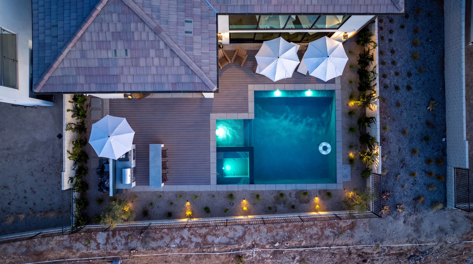 Aerial dusk view of the lit pool bordered by string lights and a climbing vine wall