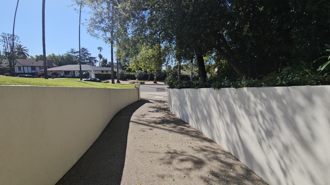 The driveway before construction: a worn dark-surfaced drive curving between the existing white stucco walls