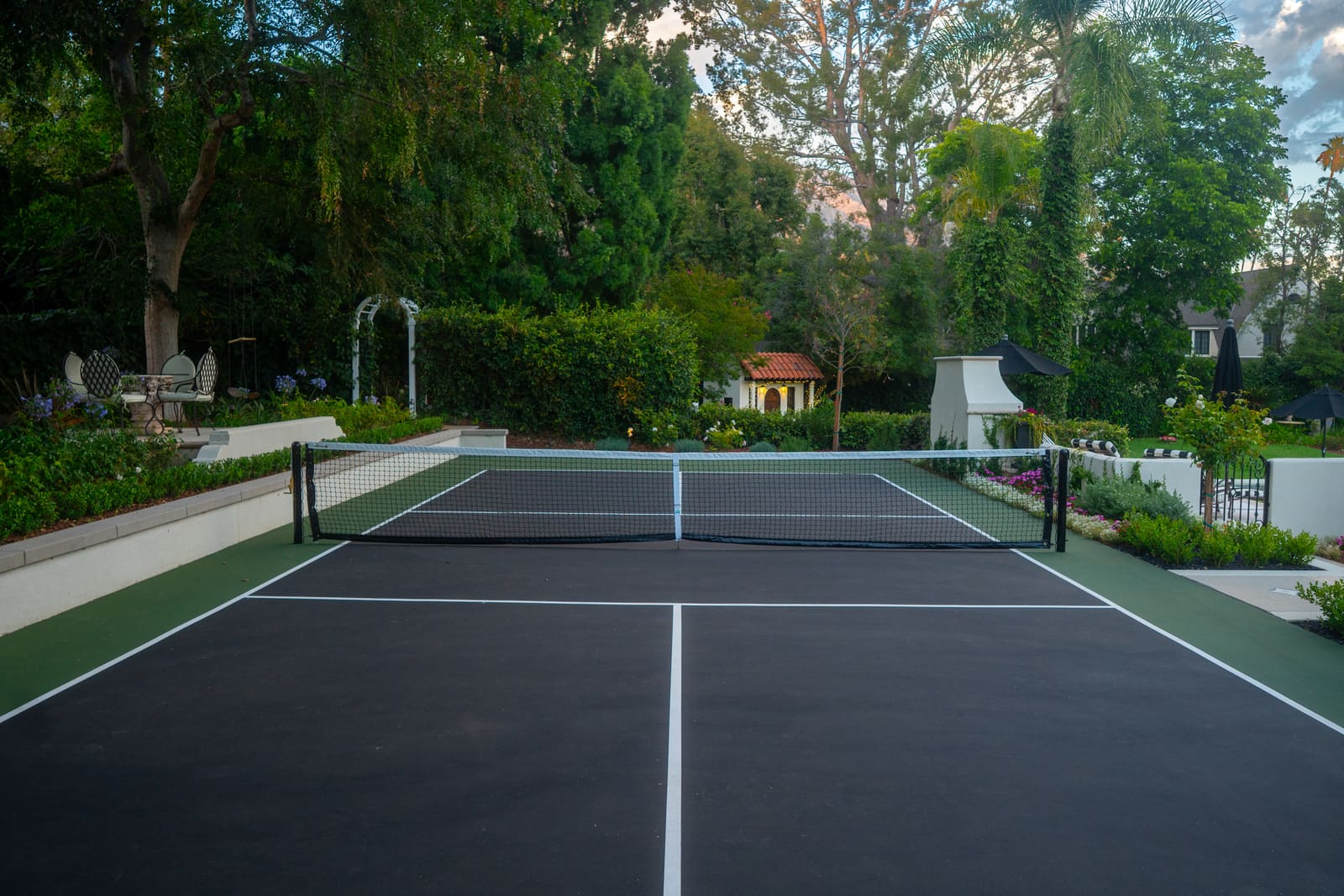 Pickleball court set into the lawn behind a clipped hedge and mature trees