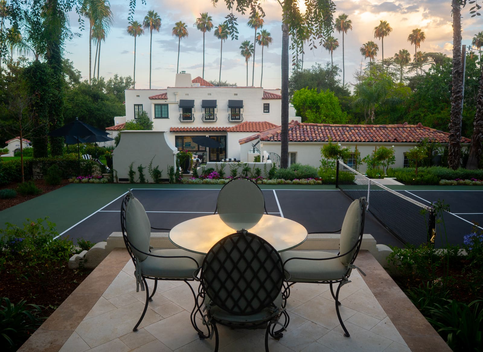 Wrought-iron table and chairs on a stone patio beside the pickleball court, lit at dusk