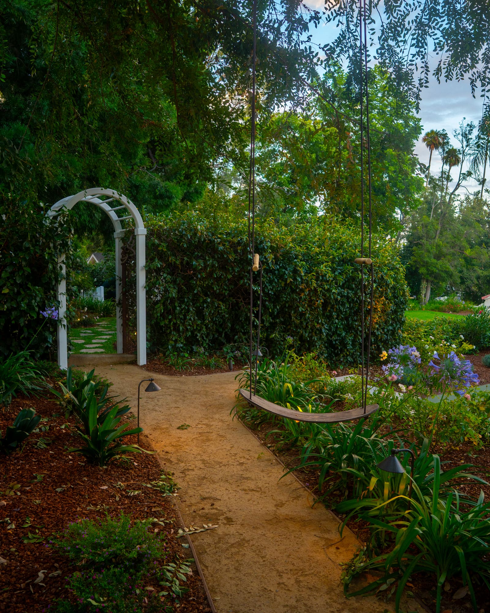 White arbor over a decomposed granite path edged with layered planting