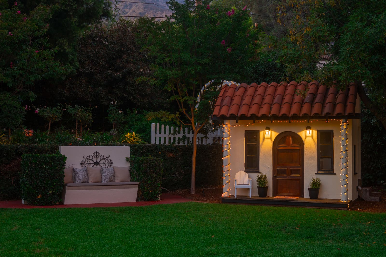 Tile-roofed pool house lit from within at dusk, seen across the lawn