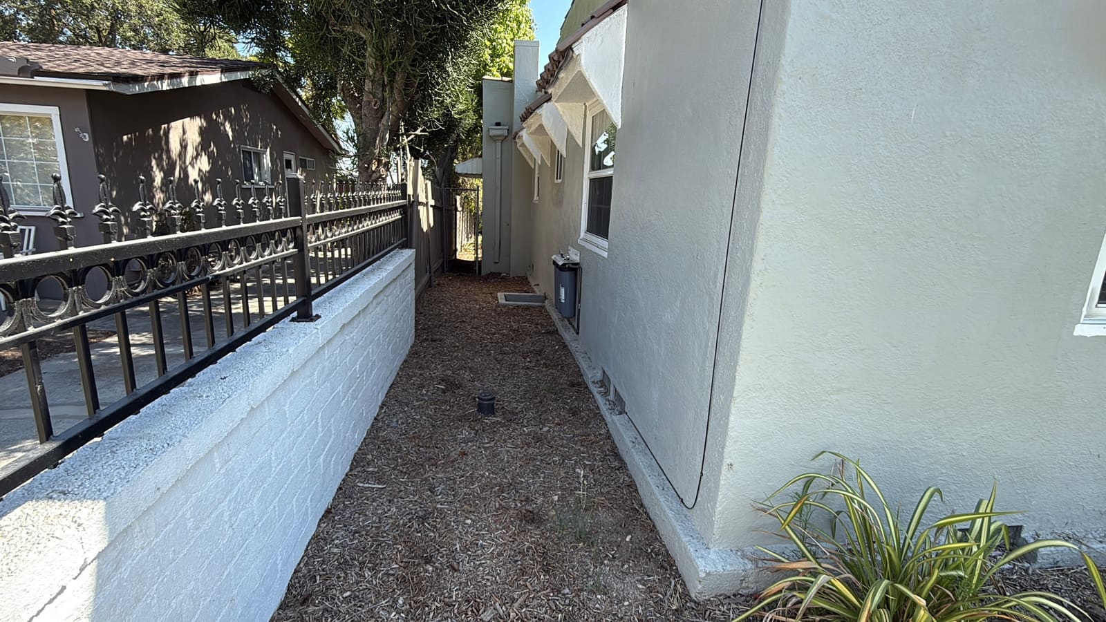 The side yard before construction: a bare dirt strip along the low wall and iron fence