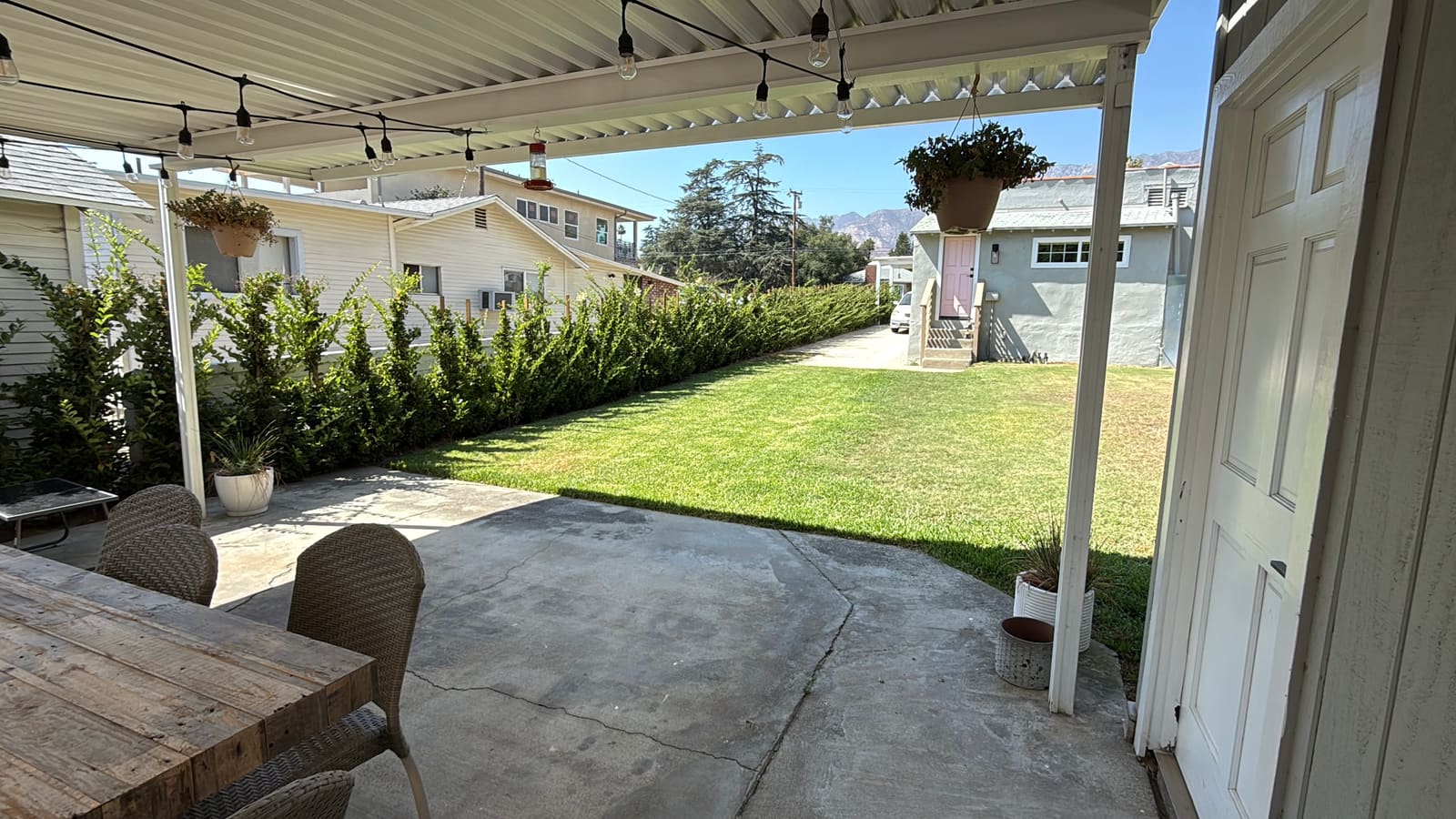 The existing covered patio and side yard before construction, hedge and lawn beyond