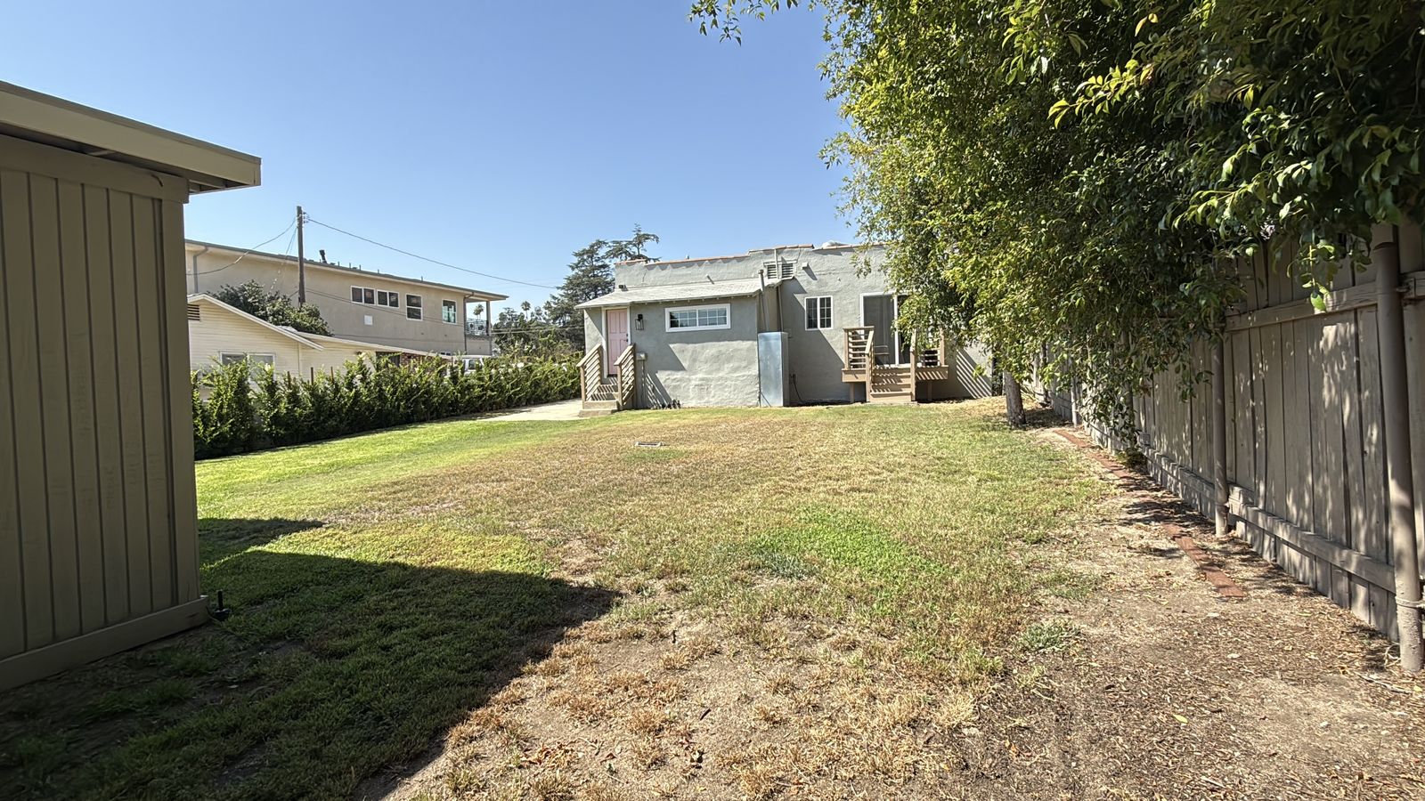 A bare backyard lawn against the fence line before any fire feature construction began