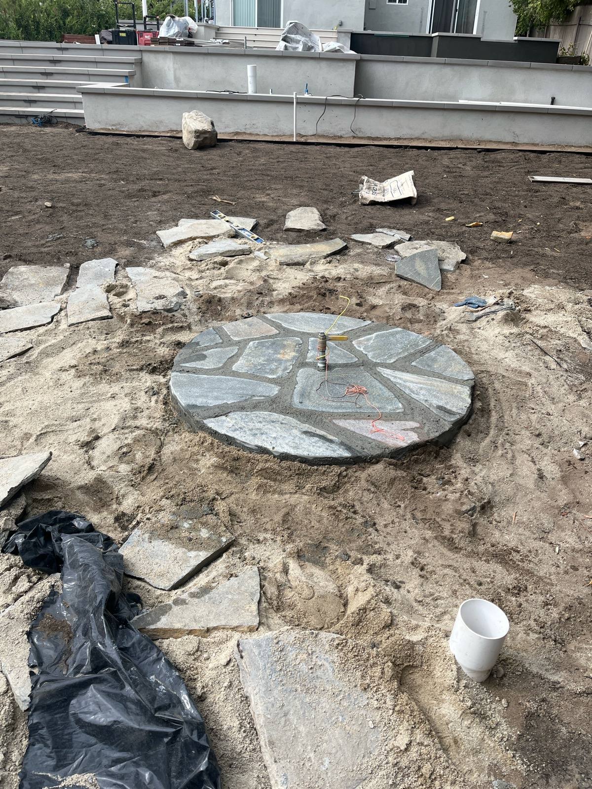 The fire pit base freshly set in flagstone with the gas line and igniter wiring in place before backfilling