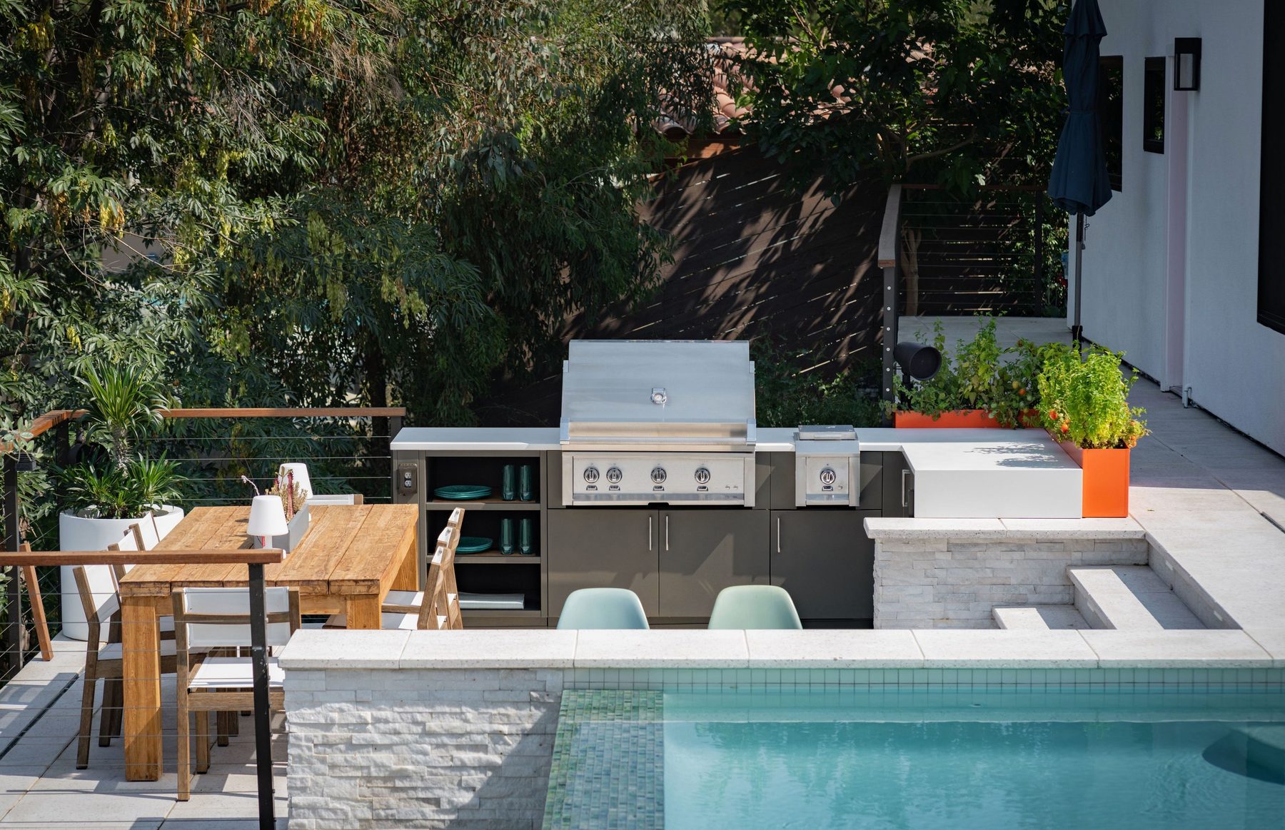 A courtyard patio with a built-in grill, dining table, and pool sharing one large-format paver space