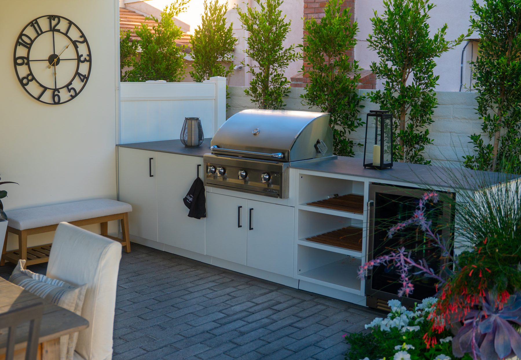 A single-run outdoor kitchen island with a grill, sink, and open shelving on a covered patio