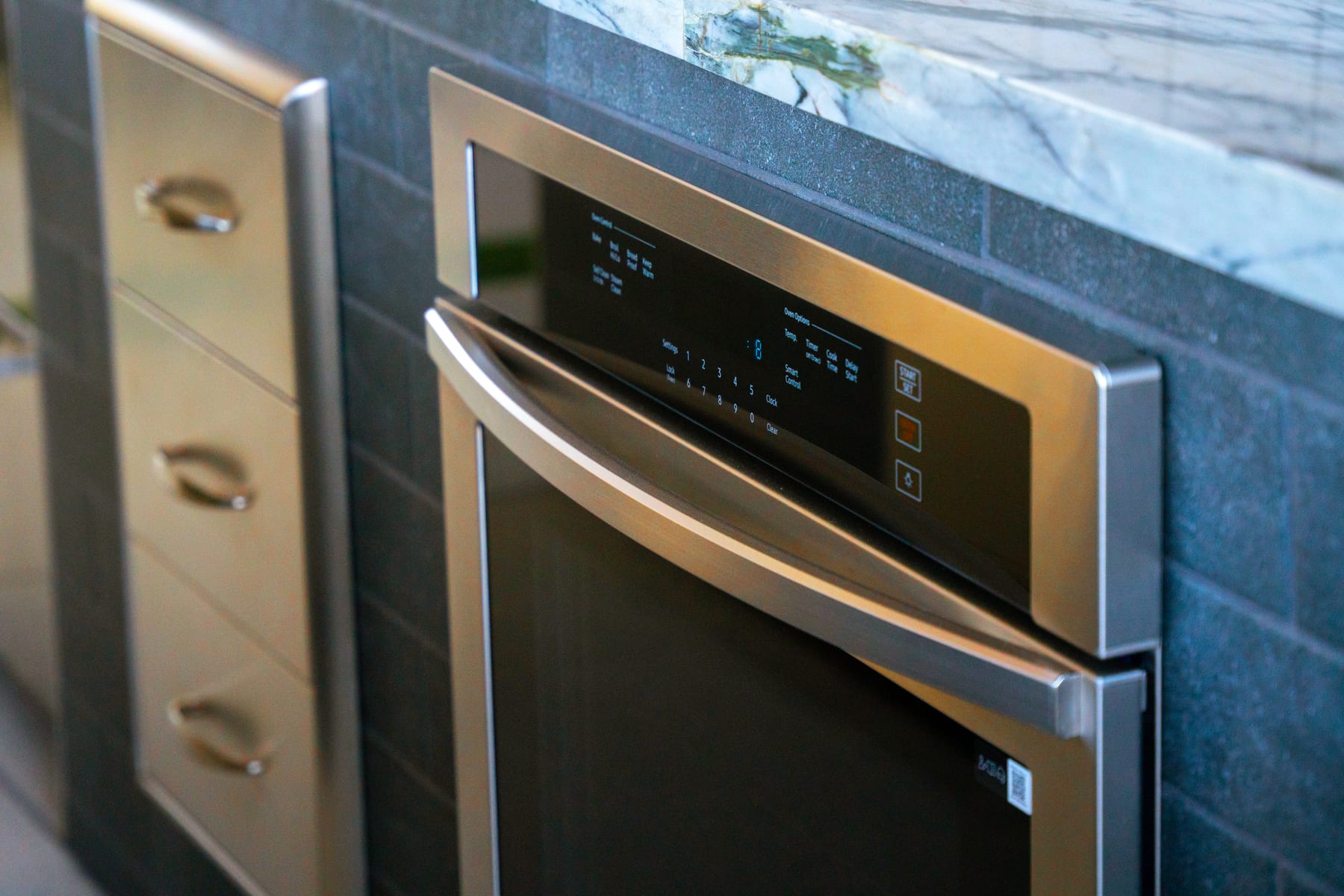 A close-up of a built-in warming drawer and appliance detail beside gold-toned cabinet drawers and a marble counter