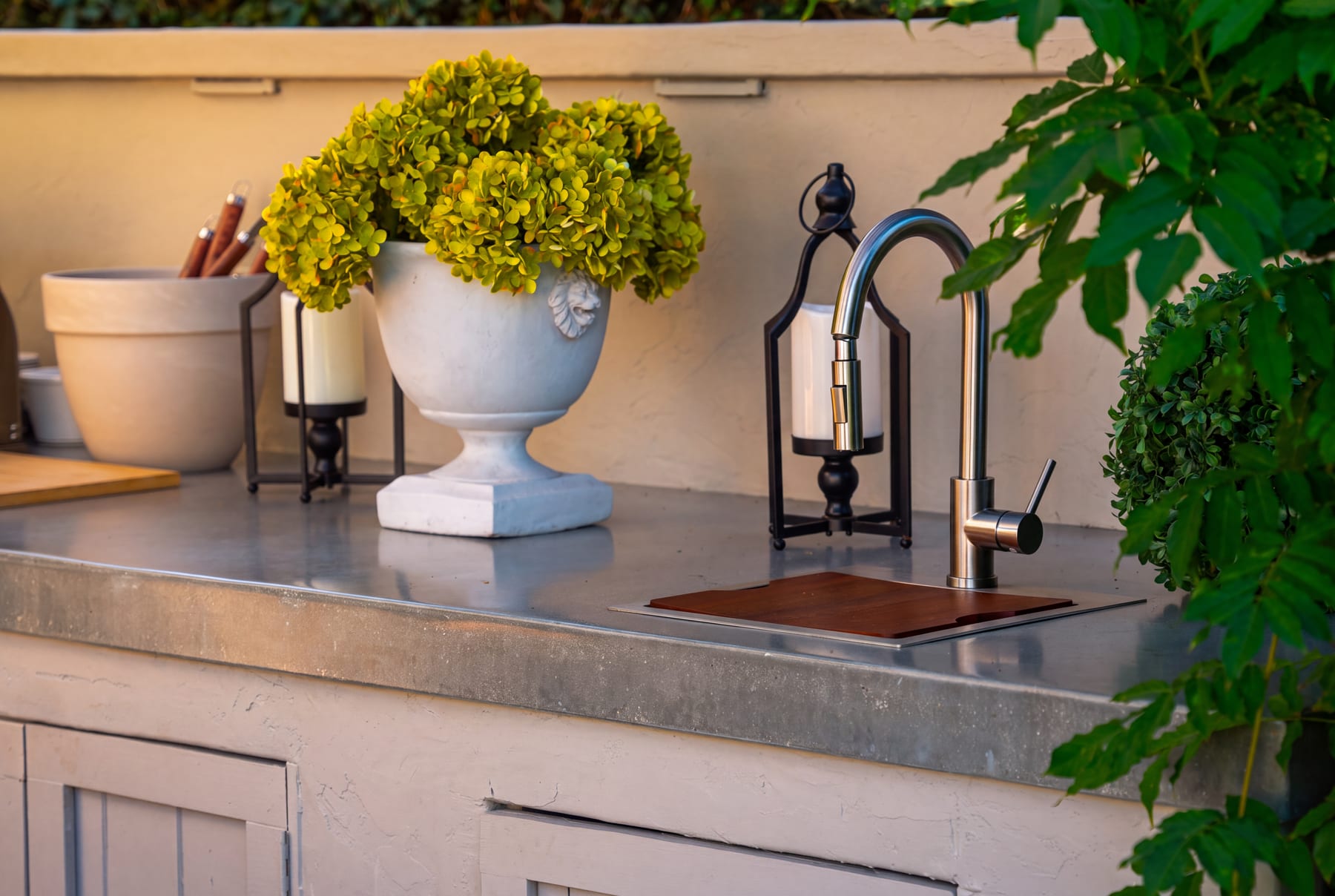 A countertop vignette with a lantern, potted greenery, and a prep sink beside a gooseneck faucet