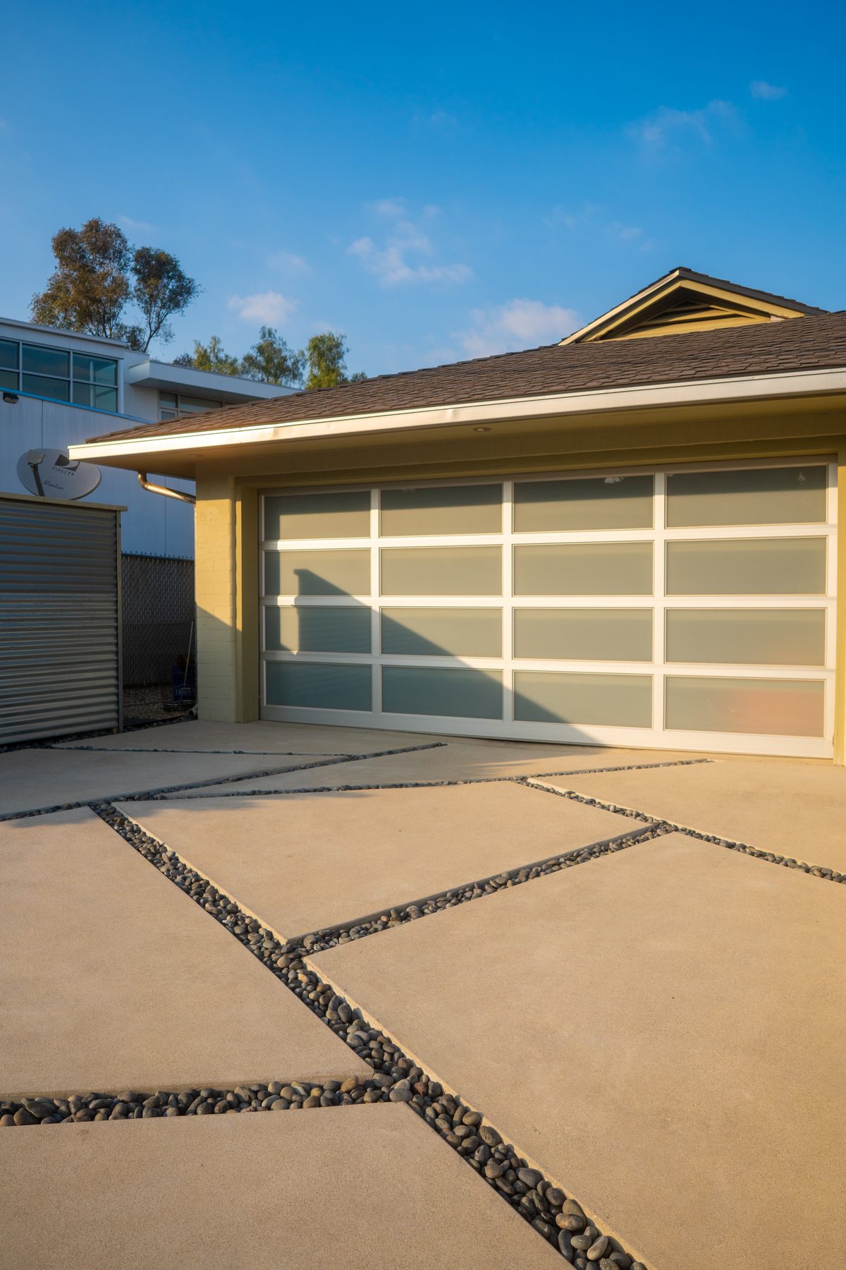 A modern driveway of large concrete slabs with pebble joints in front of a garage with frosted-glass doors