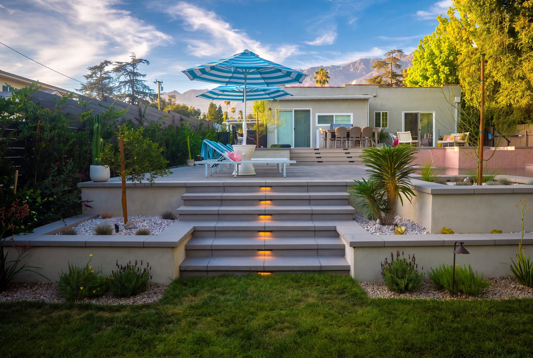 A tiered concrete-paver patio with clean-lined steps, market umbrellas, and a mountain view