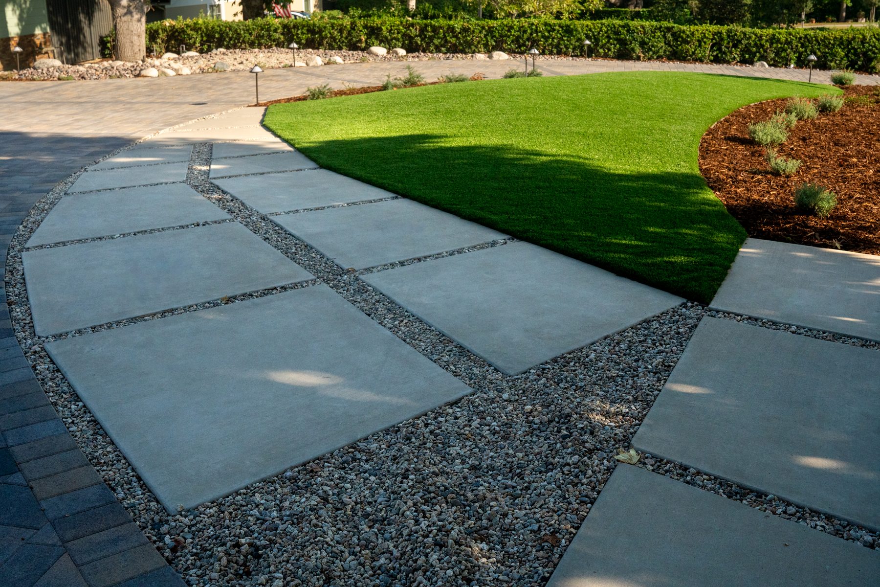 Large-format concrete pavers with gravel joints curving past a bed of artificial turf