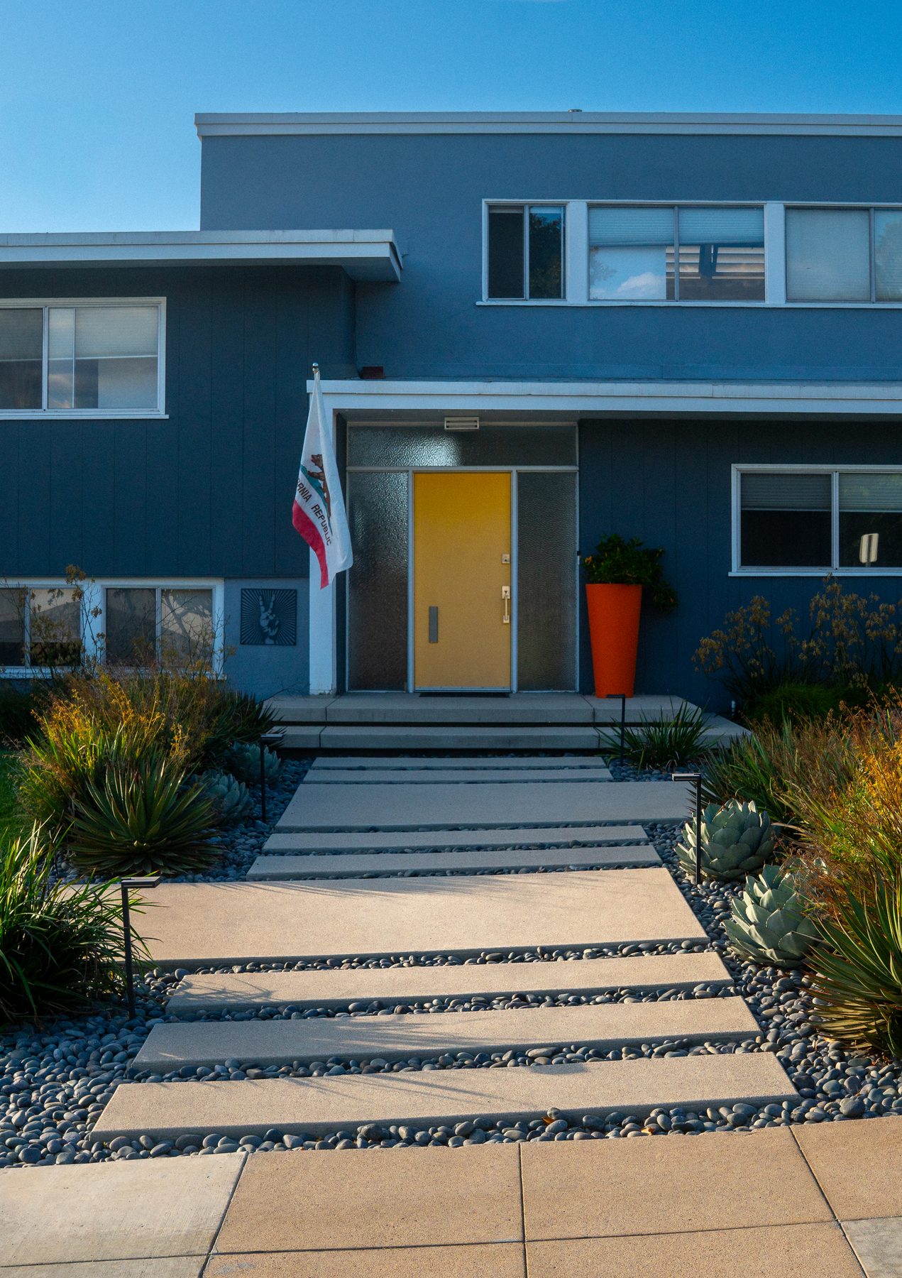 A modern front walkway of large concrete pavers with river-rock joints, framed by agave and succulent planting