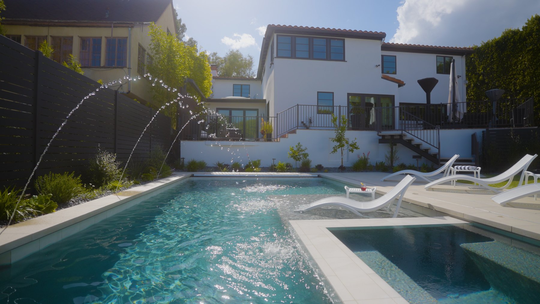 Backyard pool and raised spa with arcing water jets, lounge chairs, and a sunny patio