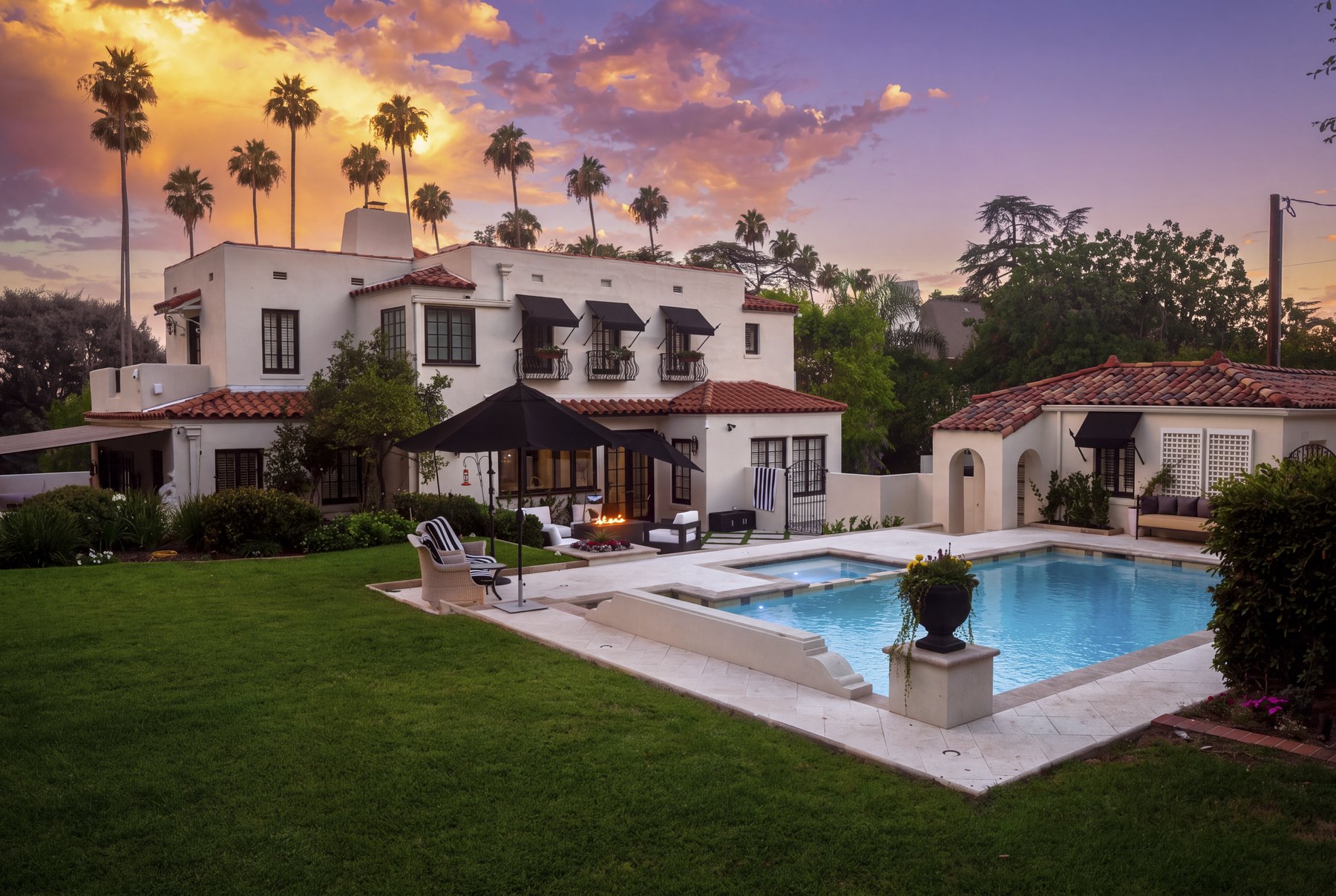 Twilight estate pool with a lawn, lounge seating, mature palms, and Spanish-style architecture