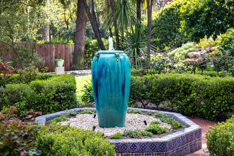 A disappearing fountain urn bubbling over river rock, set beside garden planting