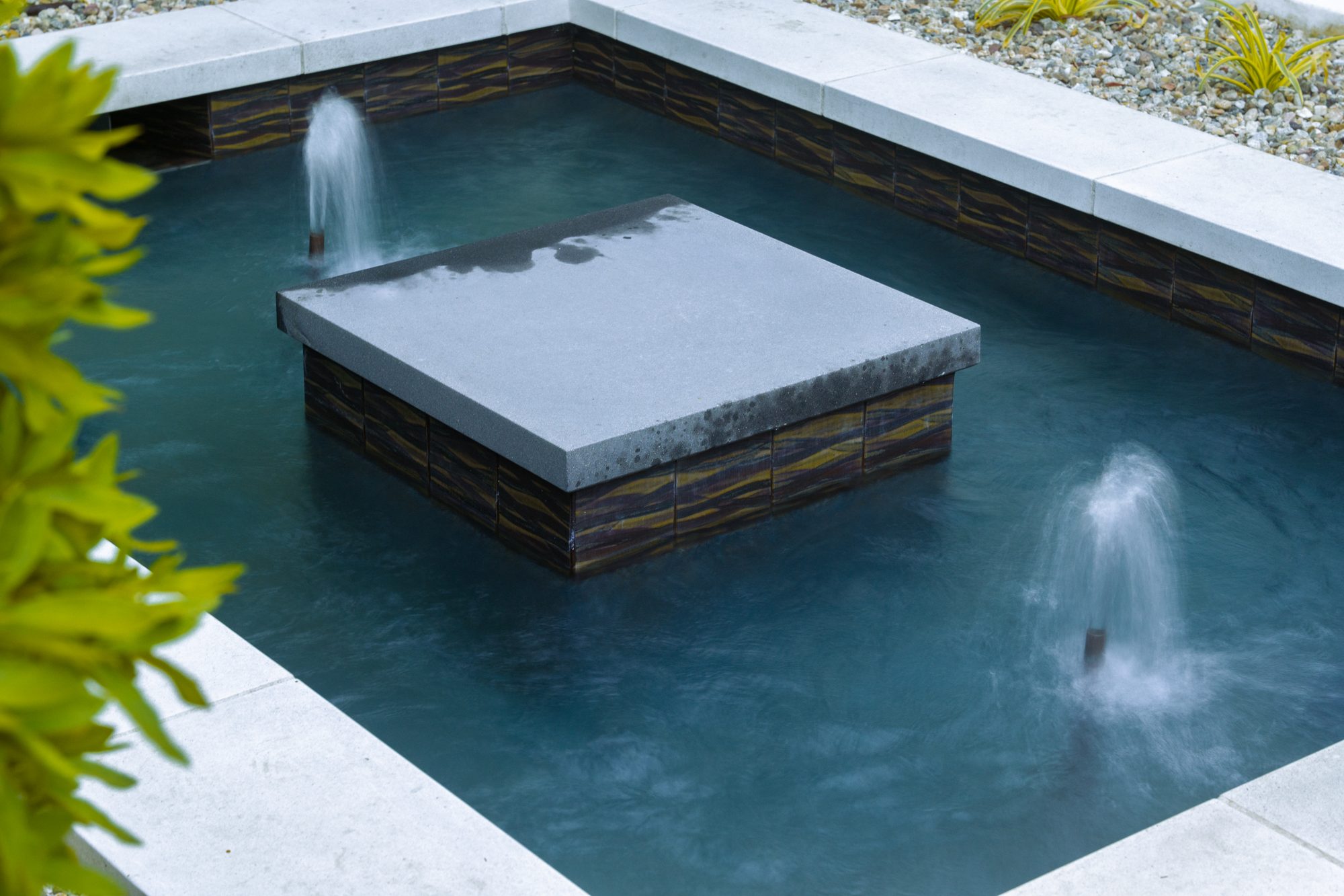 A floating stone fountain feature with jets of water in the center of a modern pool