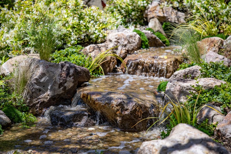 A compact pondless waterfall over stacked stone, edged with low succulent planting