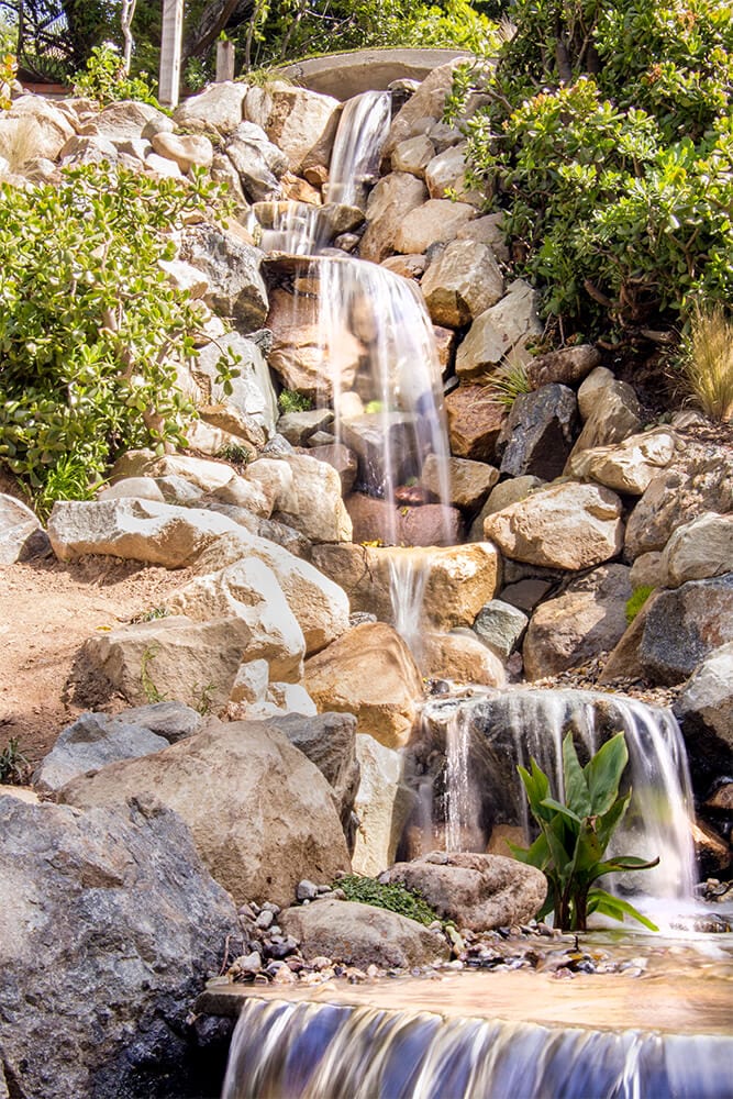 A pondless waterfall and stream set among garden planting and boulders