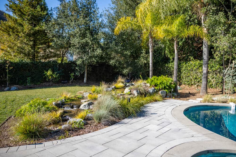 A pondless waterfall built beside a swimming pool, framed by palms and resort-style planting