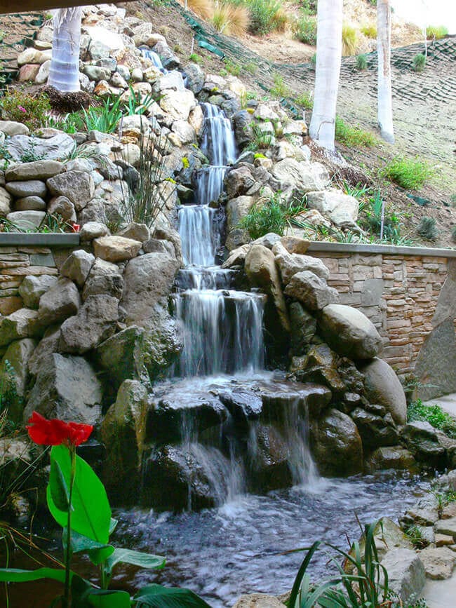 A tall multi-drop boulder waterfall set into a rugged, rock-lined hillside