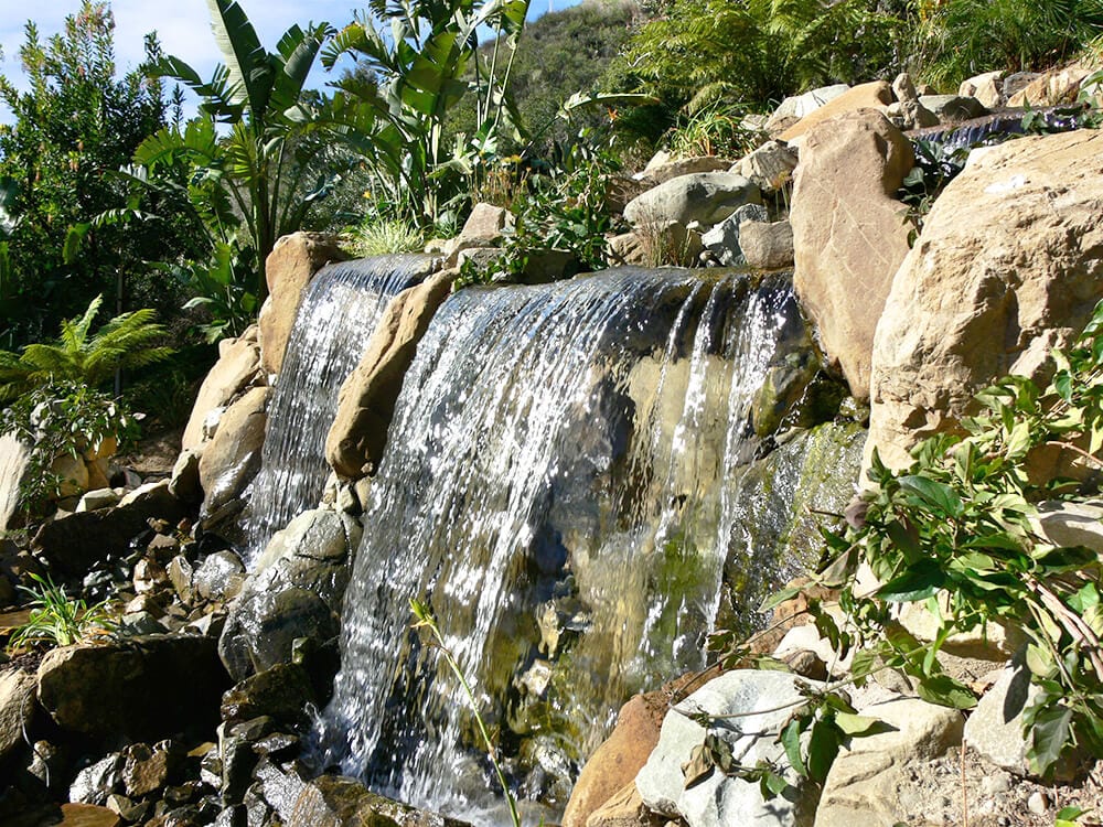 A boulder waterfall framed by mature trees and hillside planting